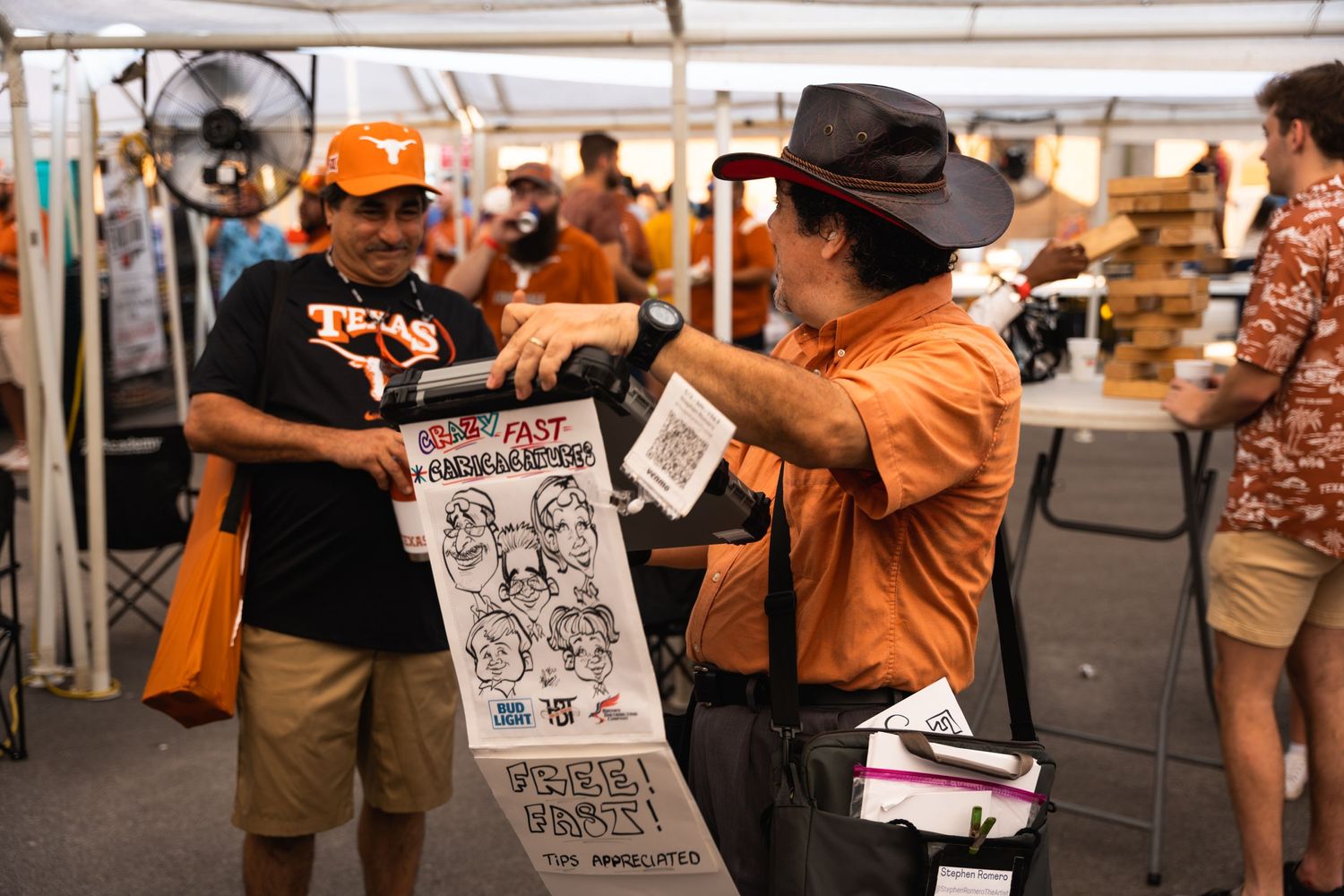 A caricature artist in an orange shirt shows his sketch to someone at an outdoor event.