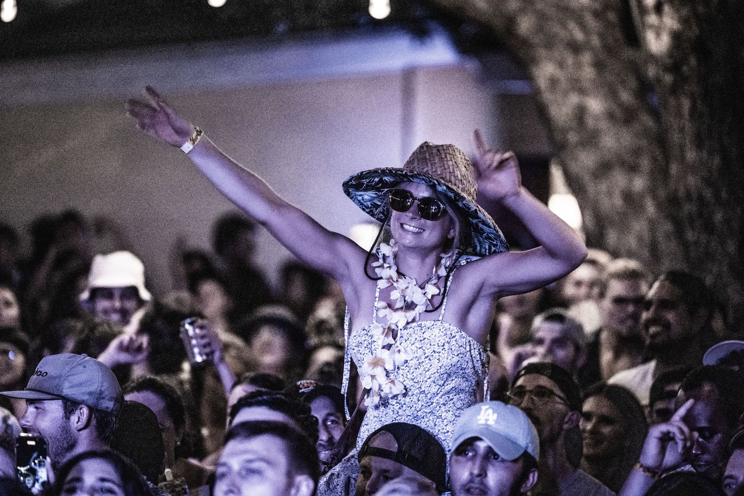 Concert goer enjoys music festival from shoulders in crowd during outdoor performance.