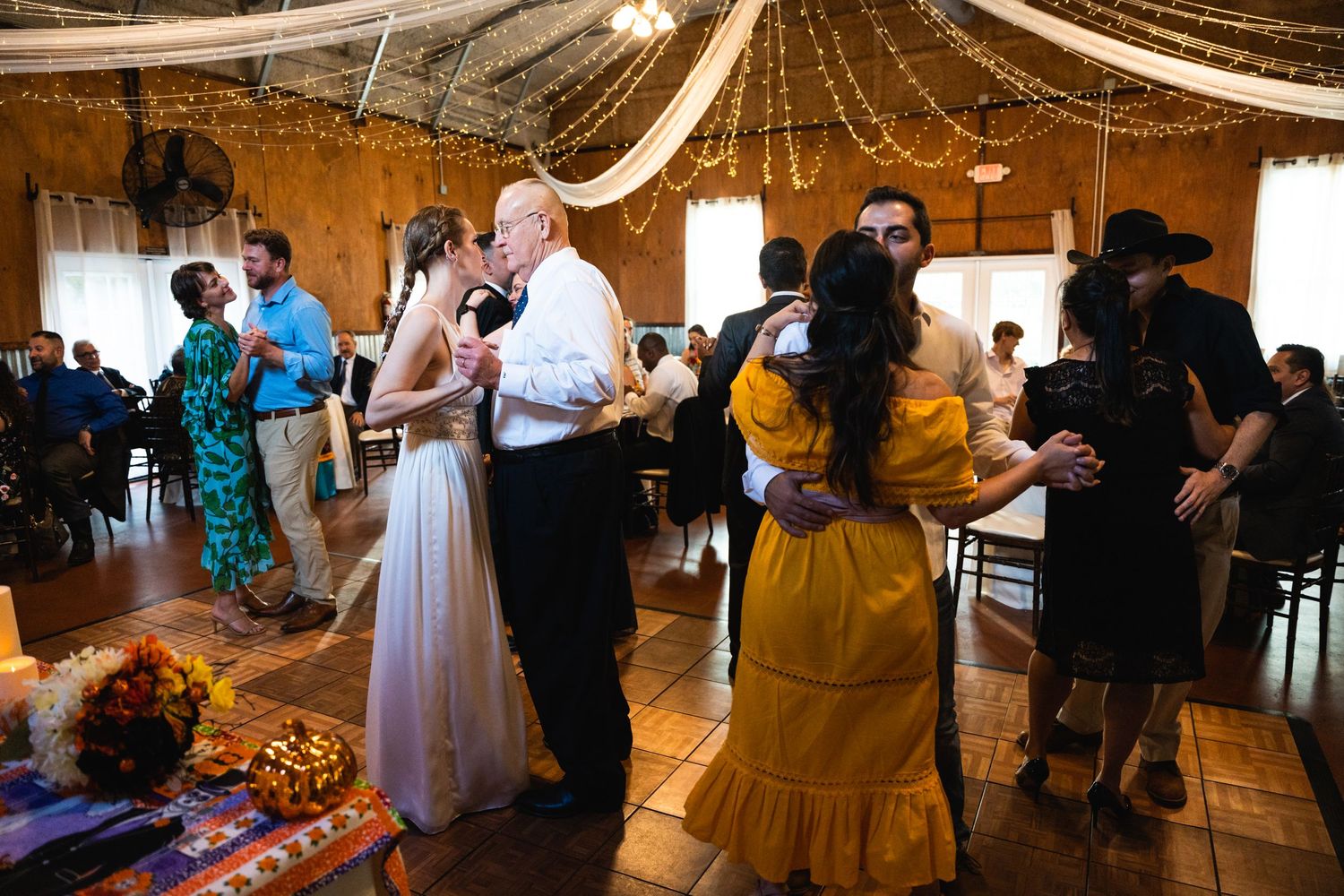 Wedding reception guests dancing together under draped fabric and string lights.