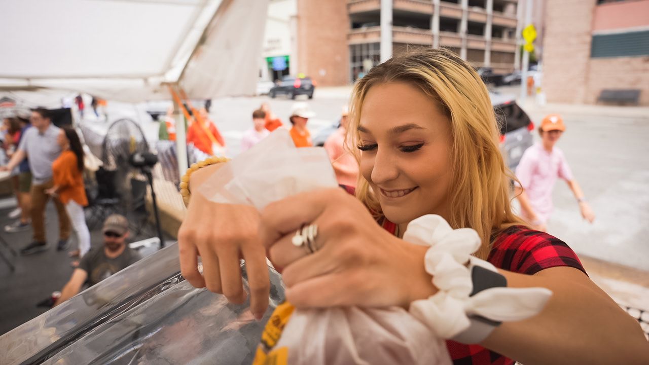 Someone carefully serving drinks at an outdoor festival table under white tent.
