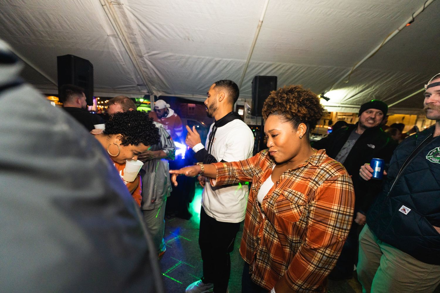 Crowd of people dancing and celebrating in dimly lit tent with colored lights.
