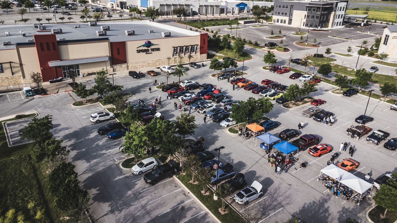 Drone shot of colorful cars arranged in a parking lot during a car show meetup.
