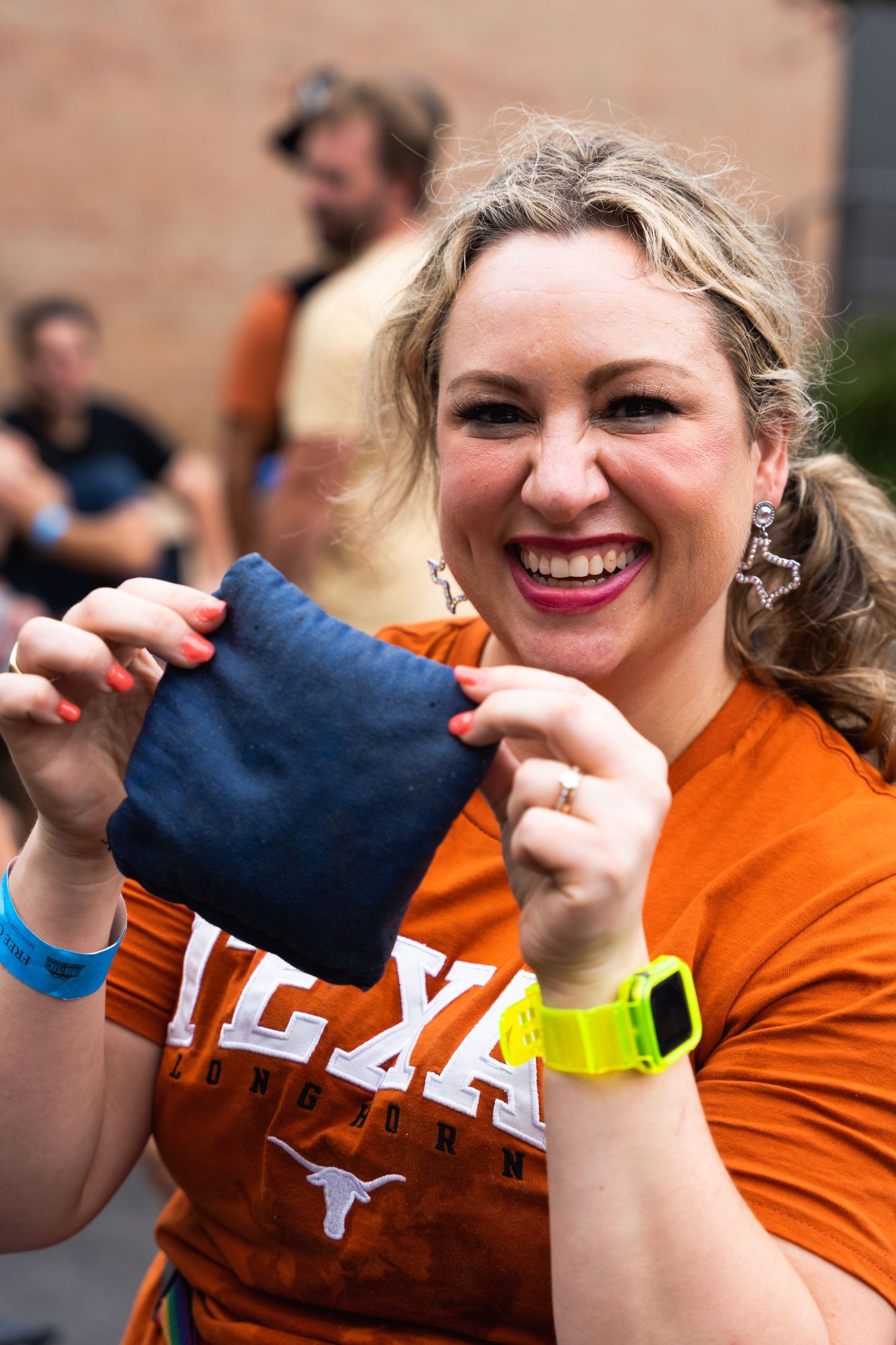 Person in orange Texas shirt excitedly holding up a blue item at an outdoor event.