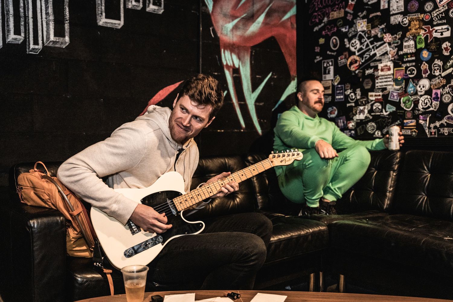 Two musicians playing guitars in a dimly lit venue with decorated walls.