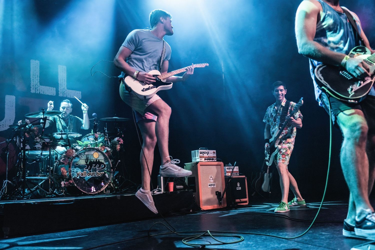 Musicians perform energetically on stage with dramatic blue lighting and amplifiers visible.