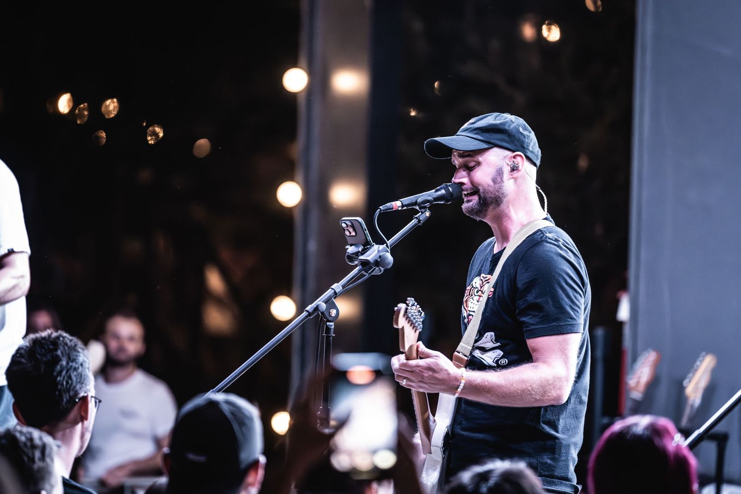 Musician plays guitar and sings into microphone during nighttime performance.