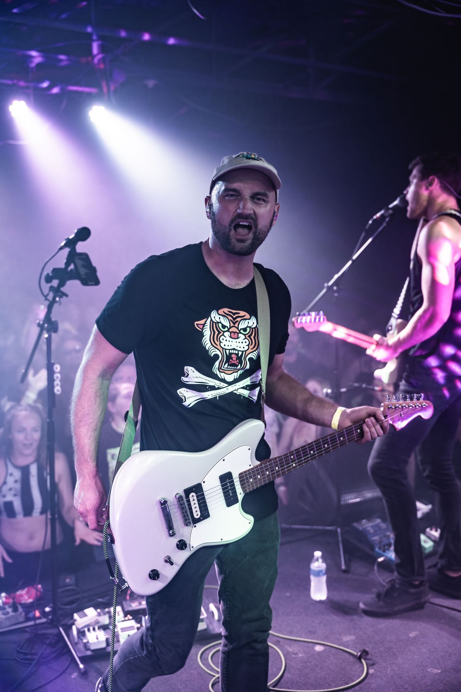 Guitarist performs energetically with a white electric guitar while wearing a t-shirt with tiger skull design.