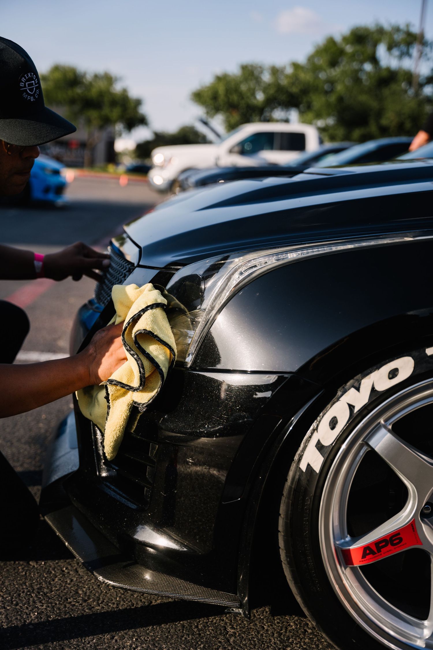 Close-up of person detailing black car with Toyo tires at car show.
