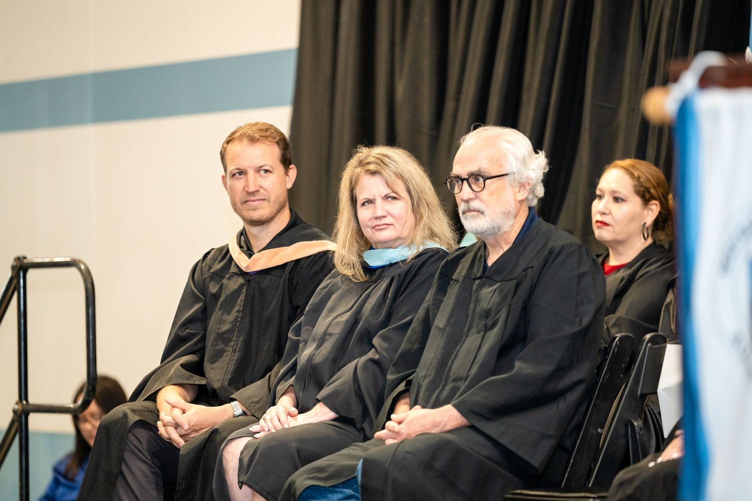 Faculty members in academic regalia seated in a row during graduation ceremony.