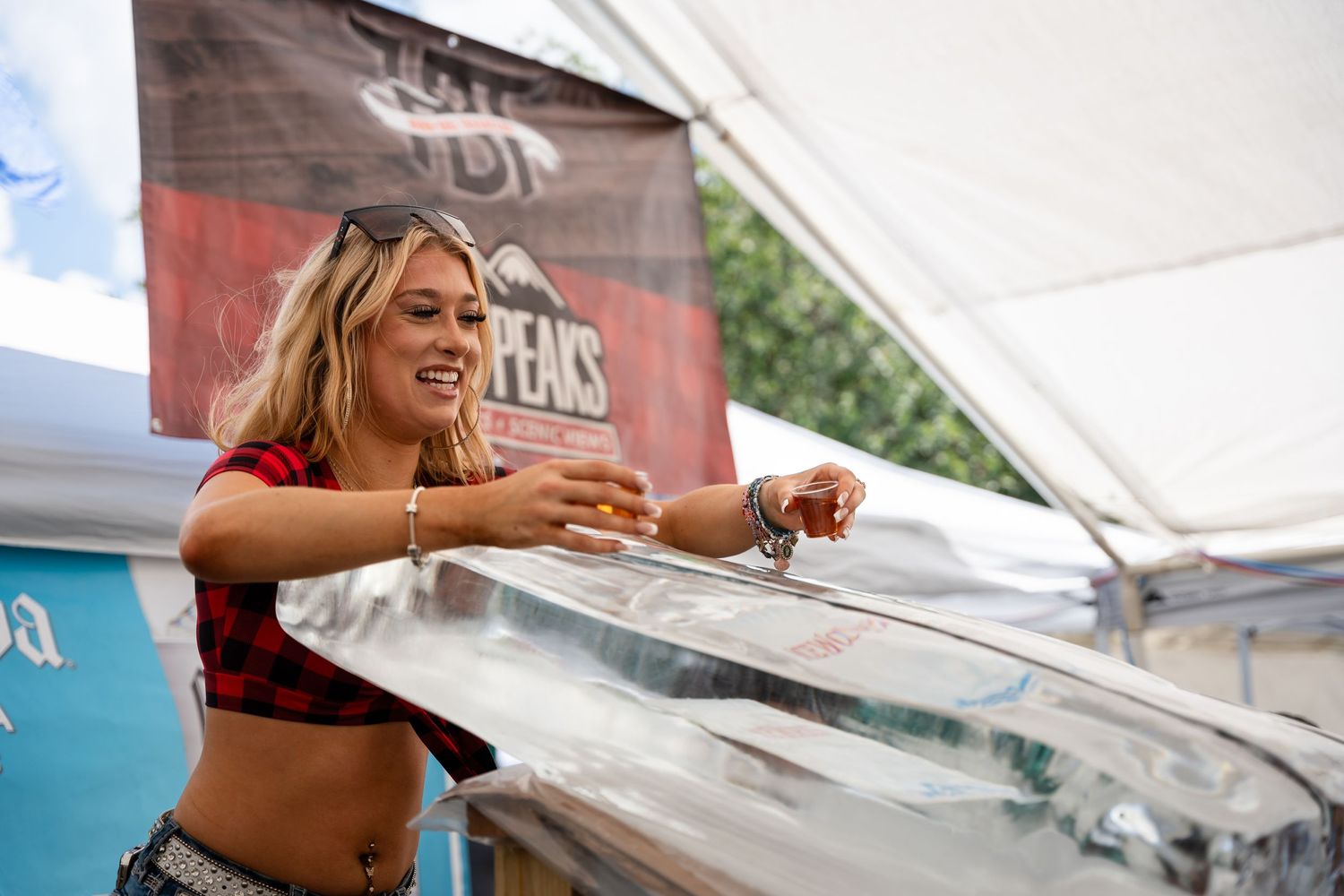 Promotional staff member serves drinks at an outdoor festival tent with Twin Peaks branding.