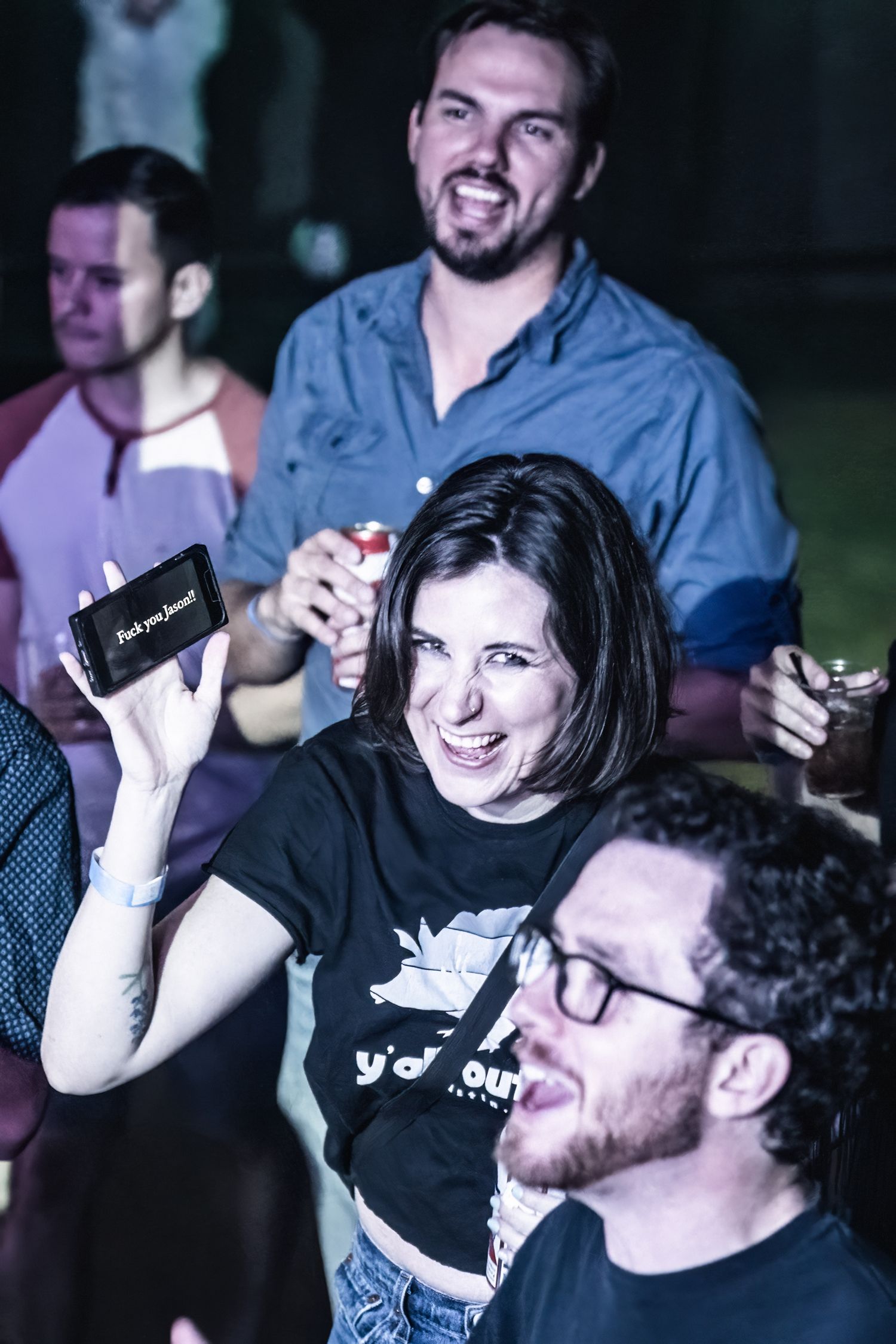 Concert attendees enjoying event with drinks and smiles under blue lighting.