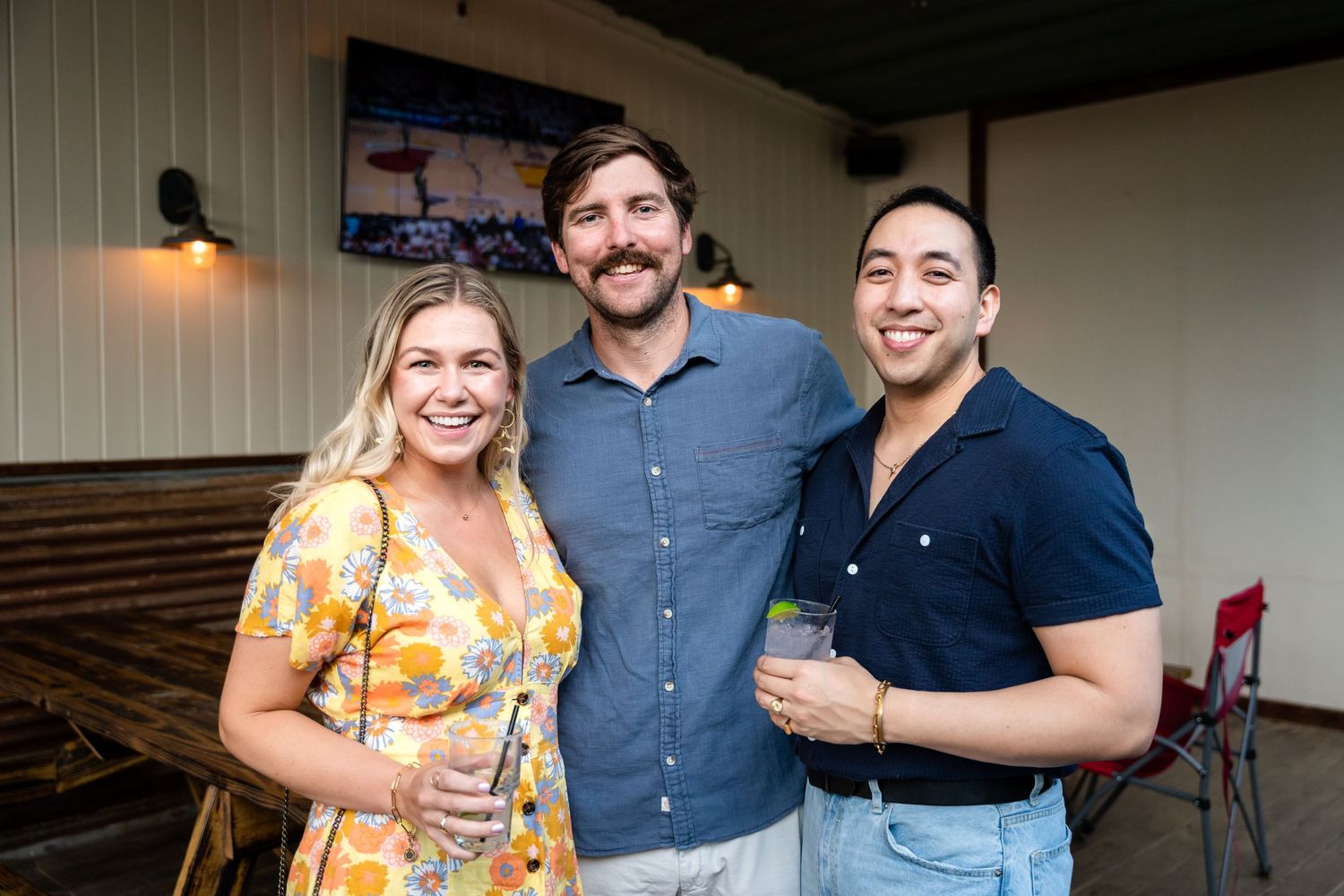 Three friends enjoying drinks together at an indoor venue with wood paneled walls.