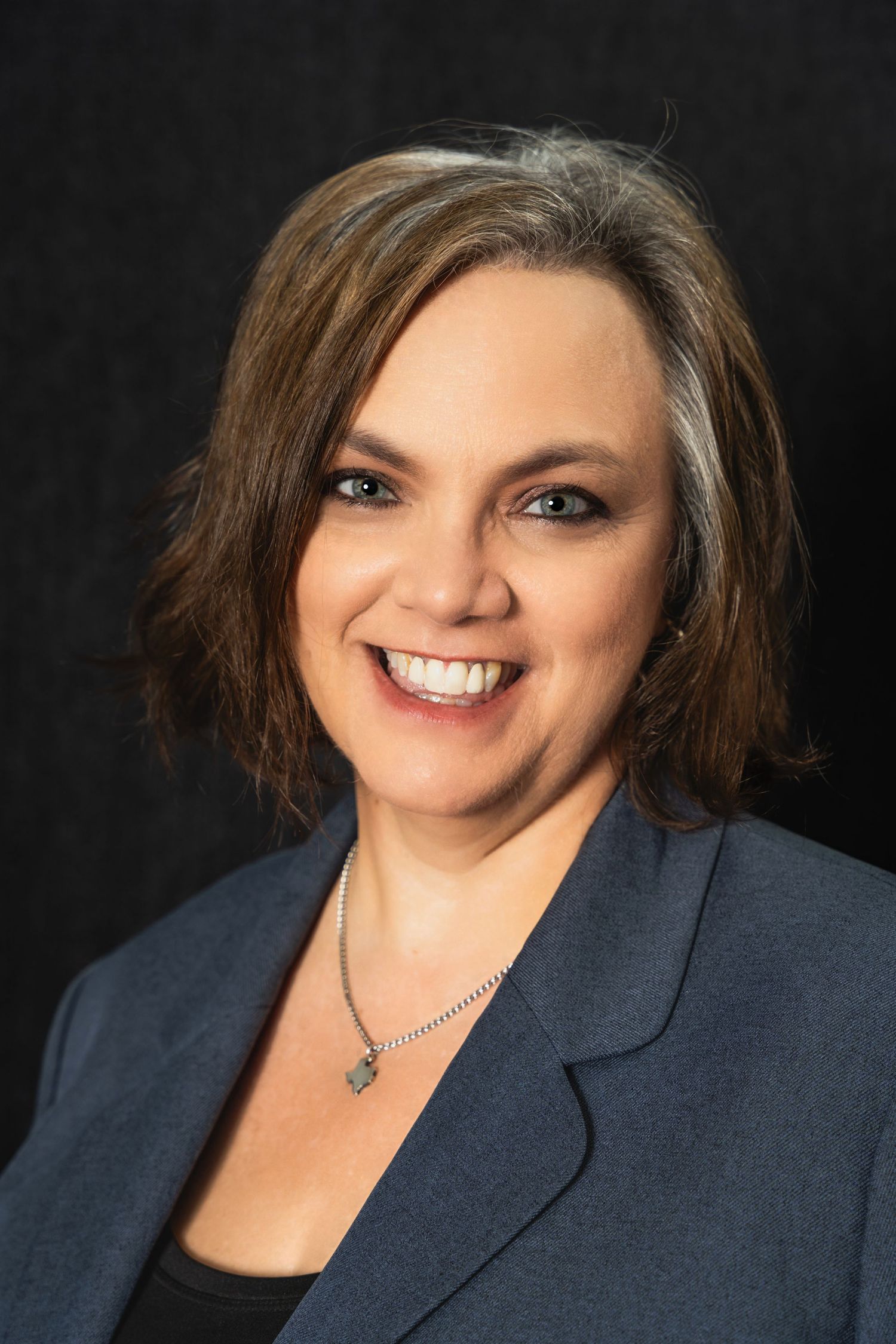 Professional headshot of a person in a navy blazer against a dark background.