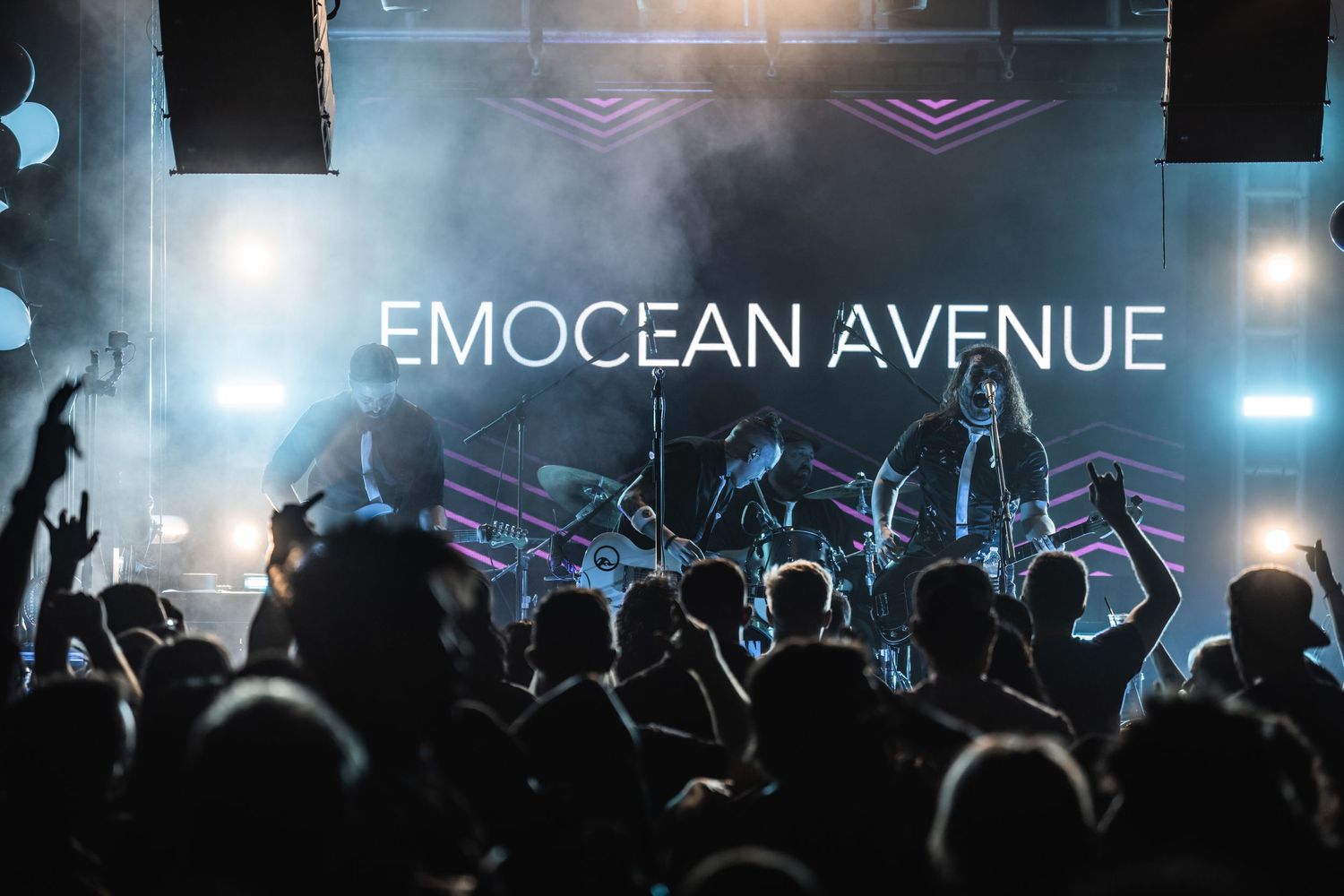 Silhouetted crowd at concert with illuminated Emocean Avenue sign and atmospheric lighting.