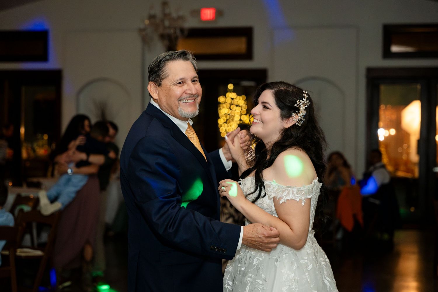 Couple dances together during a romantic wedding reception with colorful lights in the background.