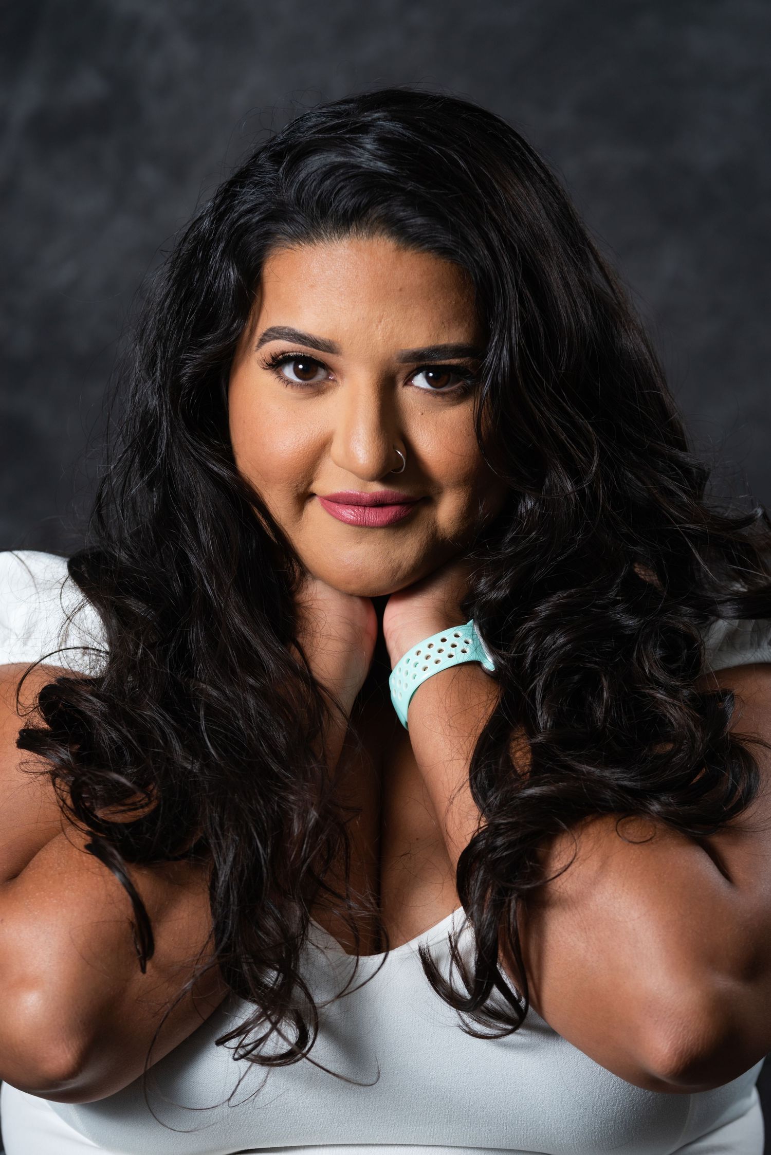 Glamour portrait with cascading dark curls and white top against dark studio background.