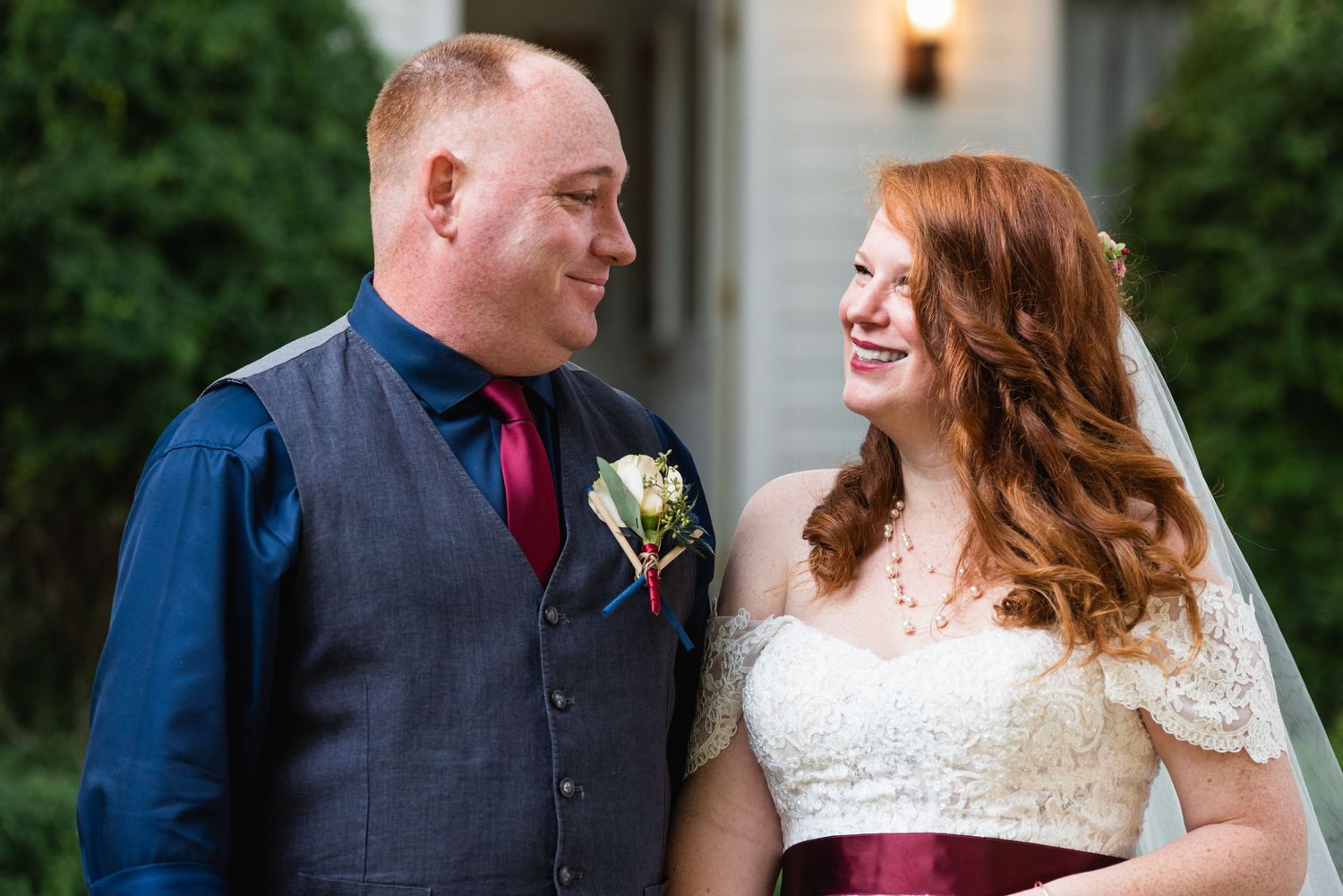 Happy newlyweds share a loving moment in front of a white building at dusk.