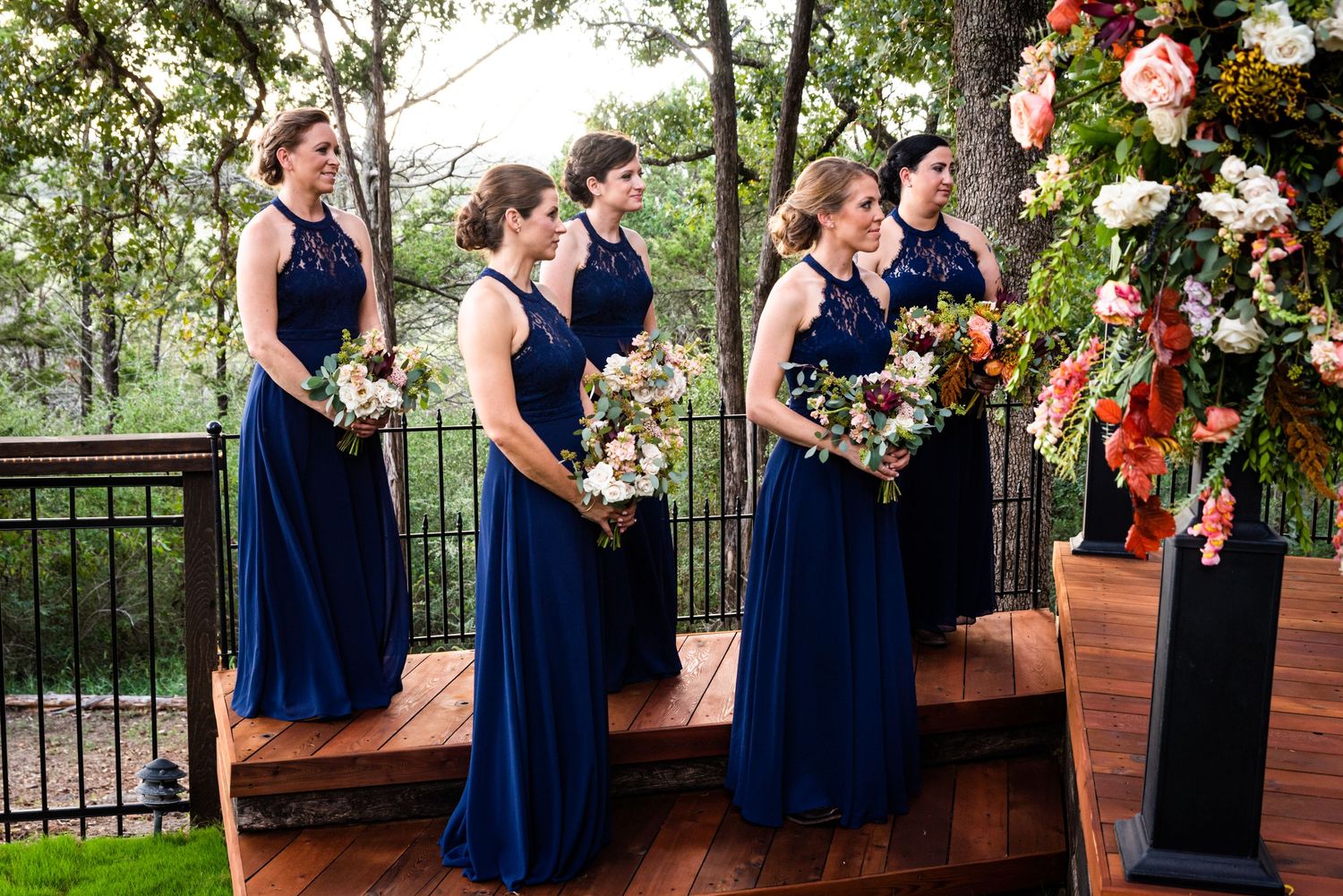 Bridesmaids in navy blue dresses hold colorful bouquets during outdoor ceremony.
