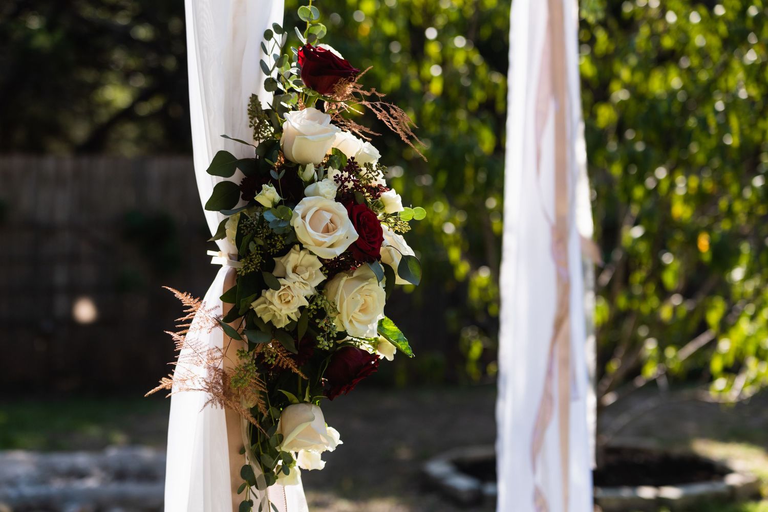 Elegant white and burgundy floral arrangement decorating an outdoor wedding arch.