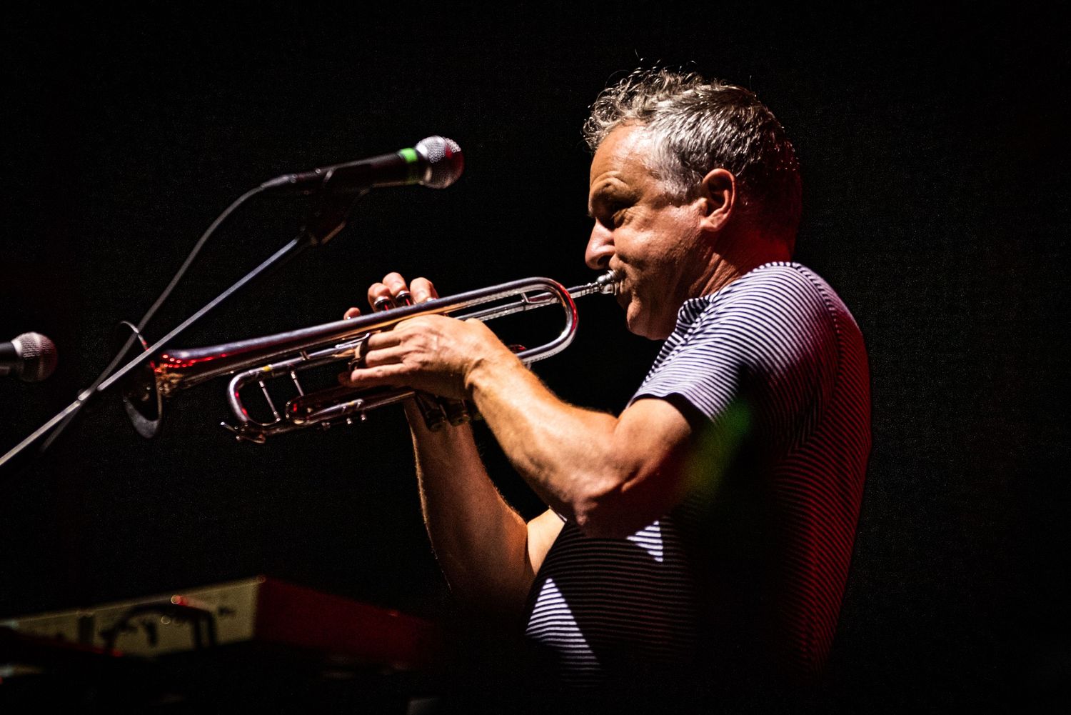 A trumpet player performs on stage in dramatic lighting with microphones visible.