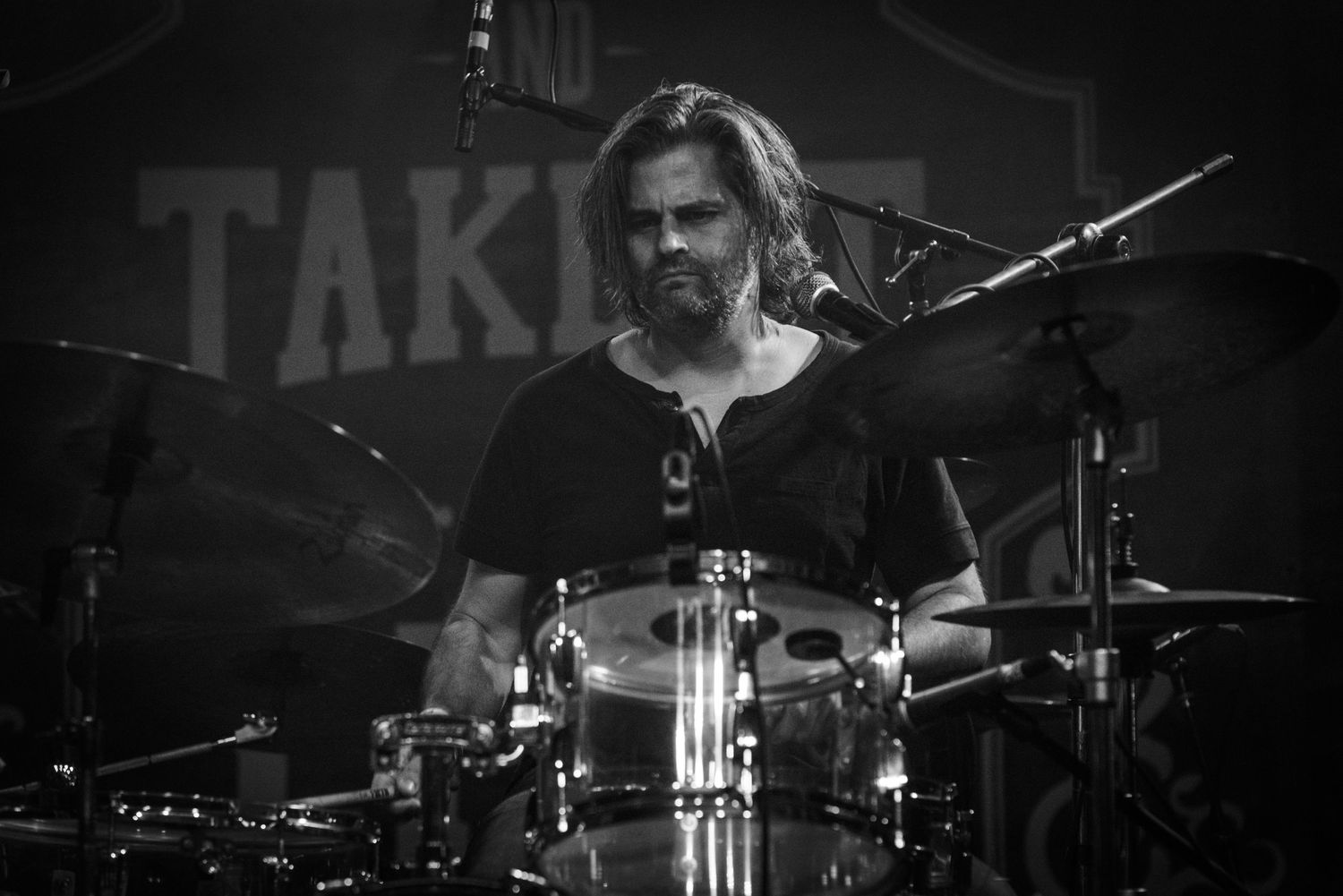 A drummer performs passionately behind a drum kit on stage with dramatic lighting.