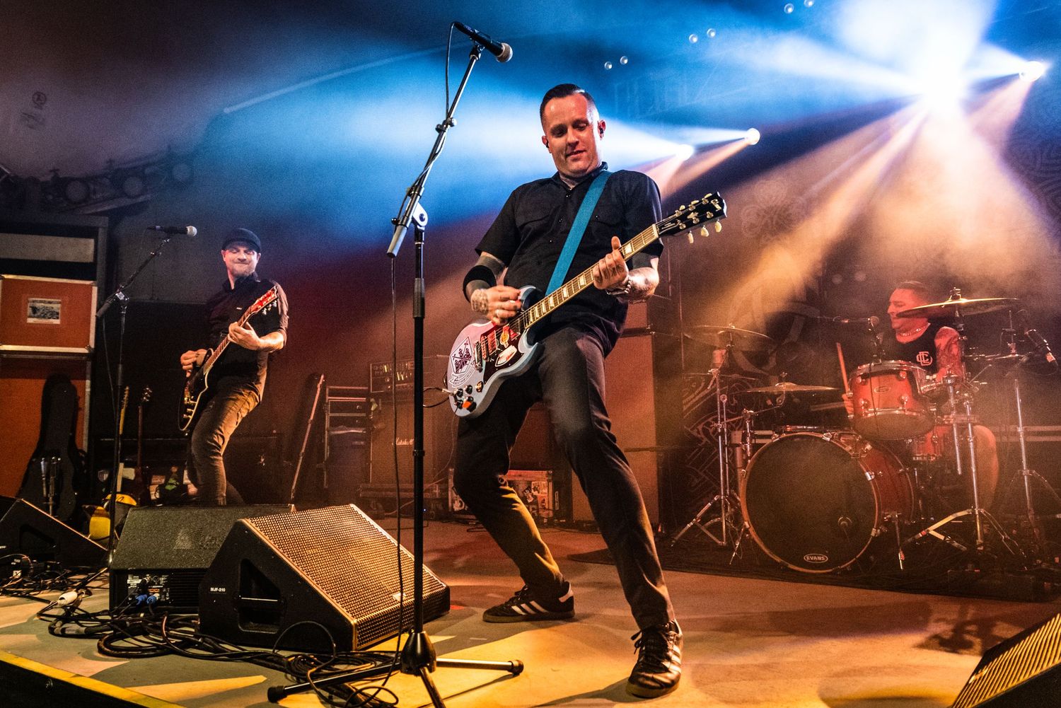 Musicians perform on concert stage with dramatic orange lighting and fog effects in the background.