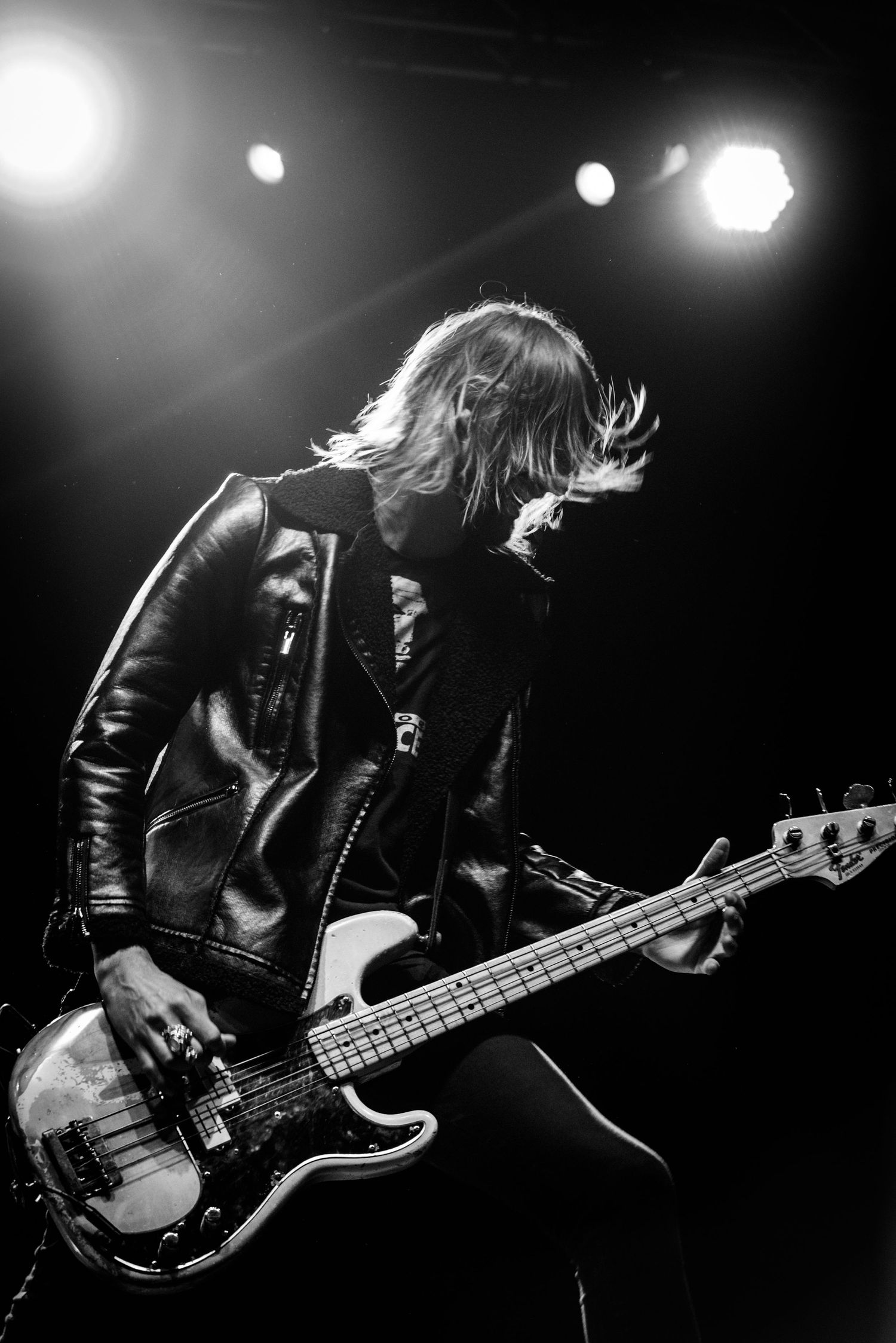 Energetic bassist in leather jacket performing on stage with dramatic concert lighting.