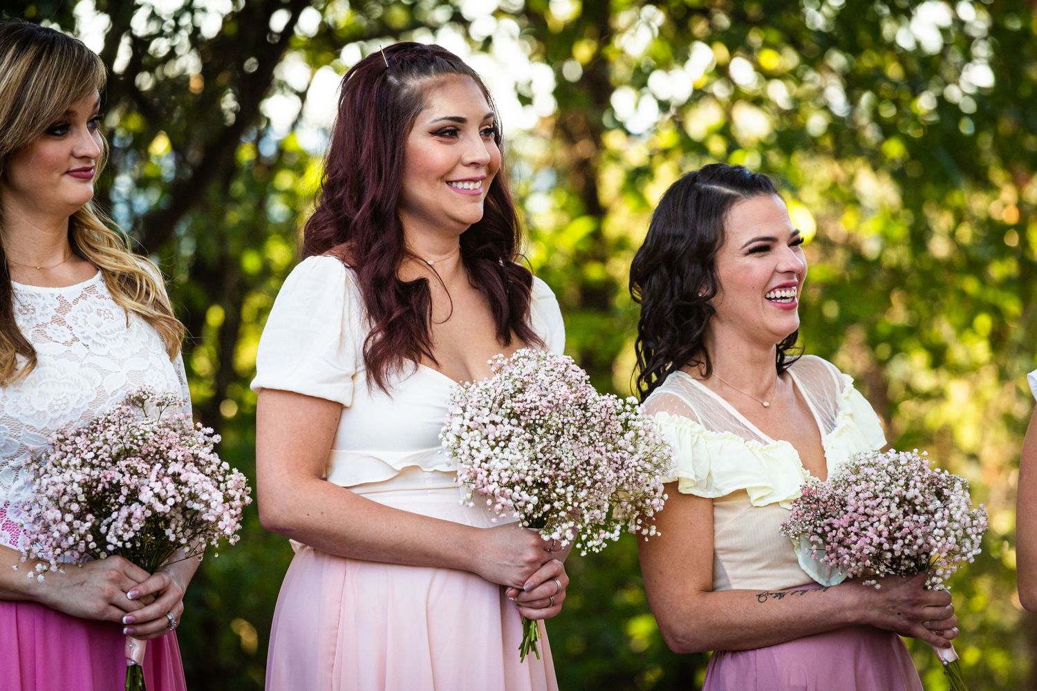 Bridal party holding baby's breath bouquets wearing pink dresses at outdoor ceremony.