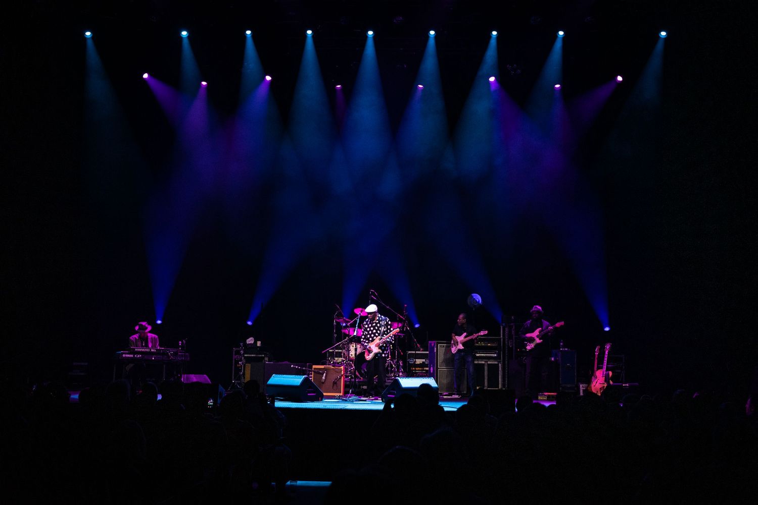 Silhouetted band performs under dramatic blue stage lighting array.