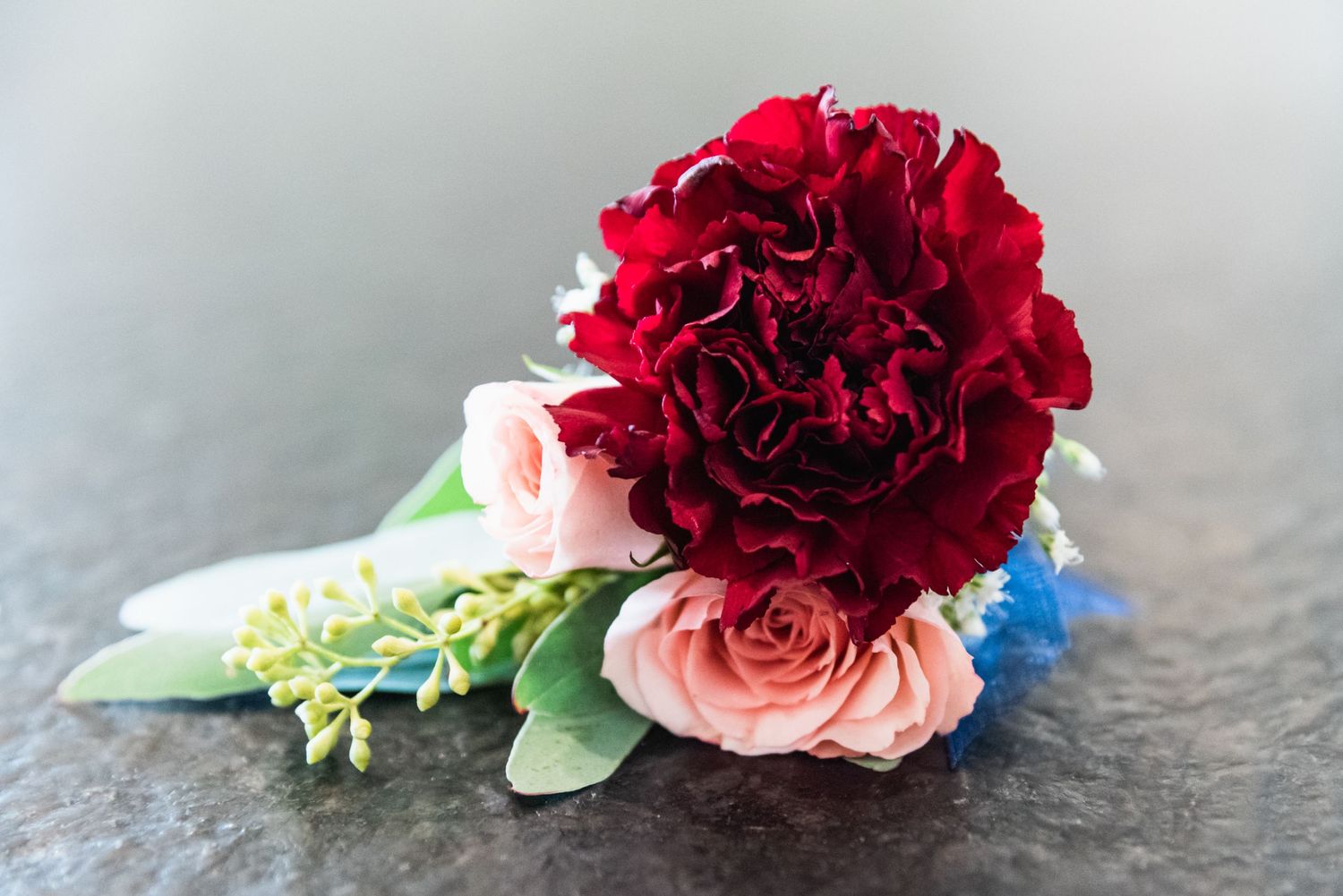 A vibrant red carnation with pink roses and blue accents arranged as a wedding floral piece.