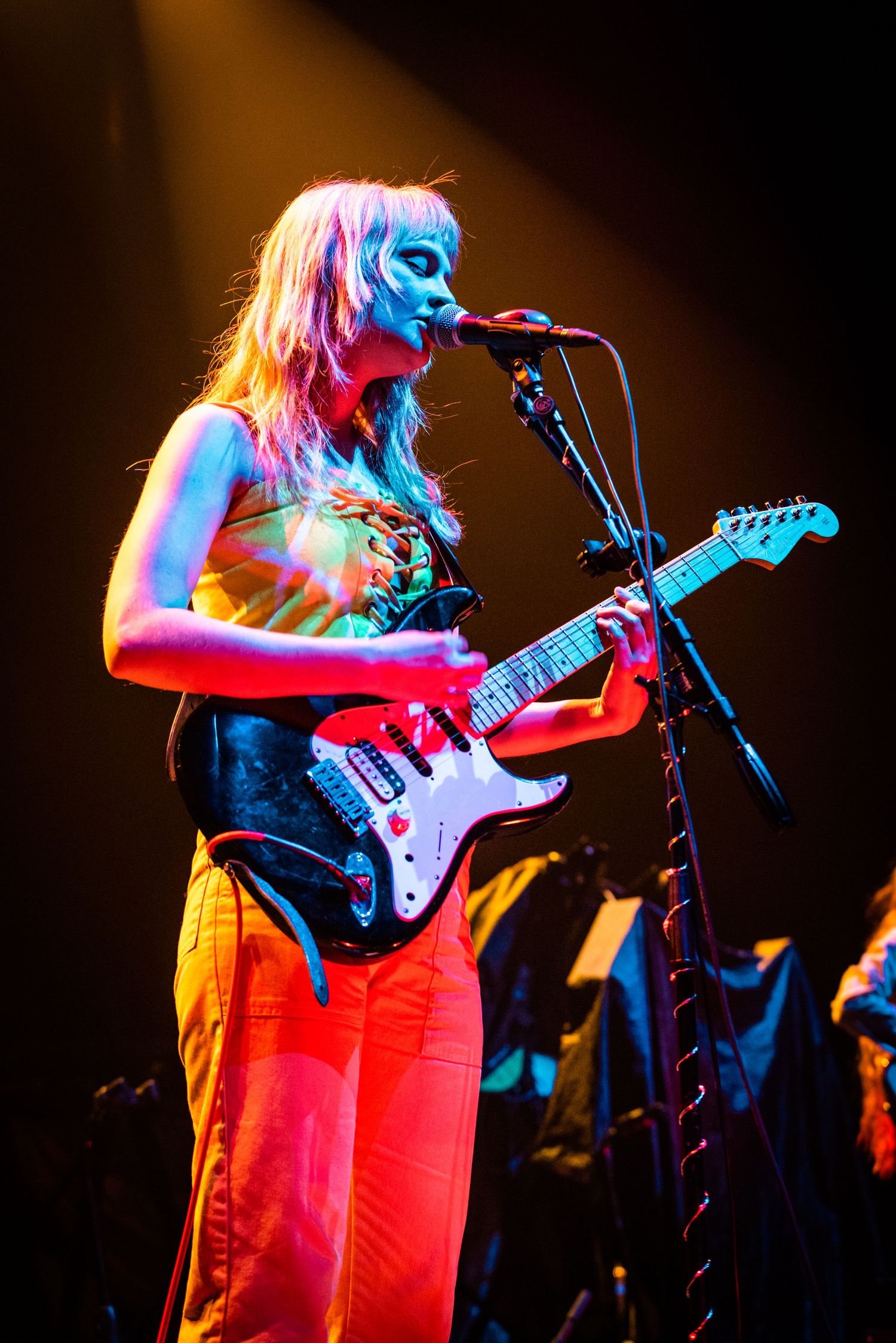 Musician in dramatic lighting performs with an electric guitar and microphone on stage.