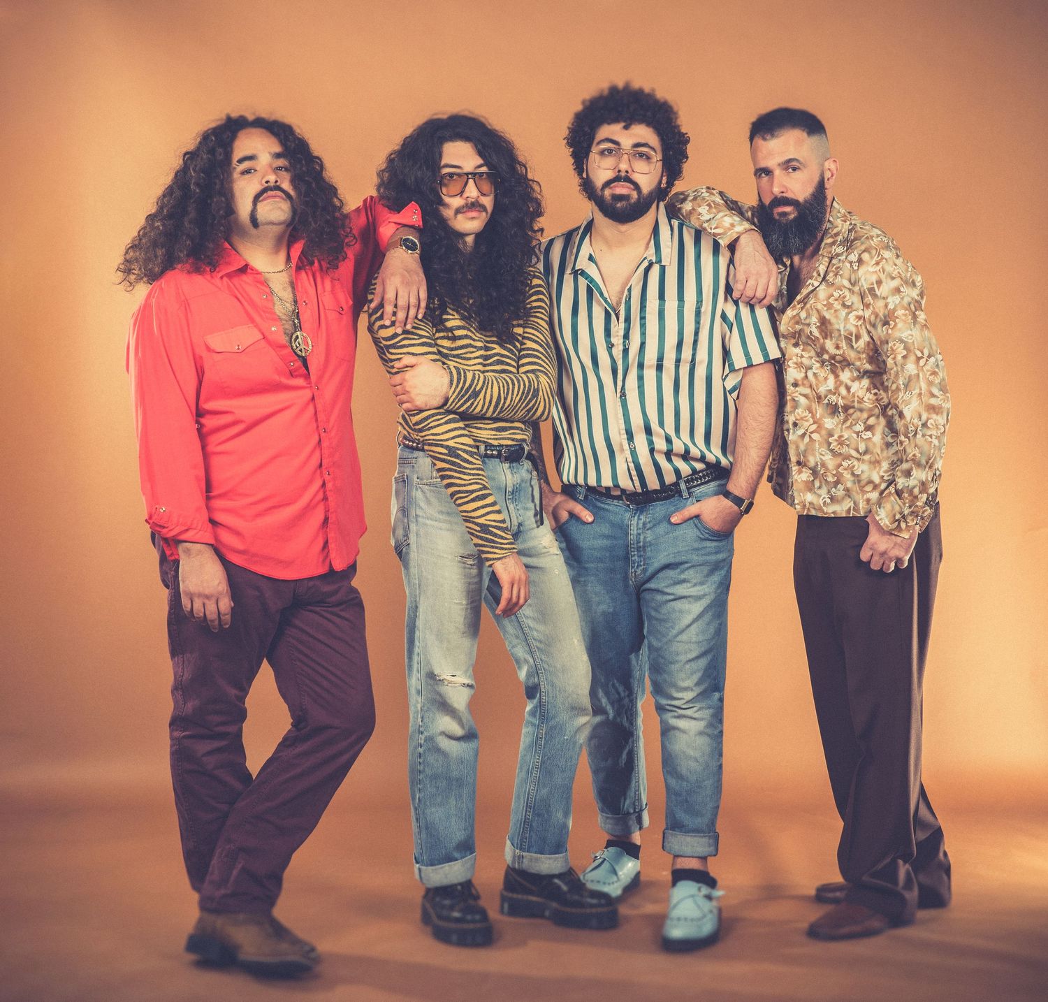Group of musicians in vintage-inspired clothing posing for studio portrait with warm lighting.