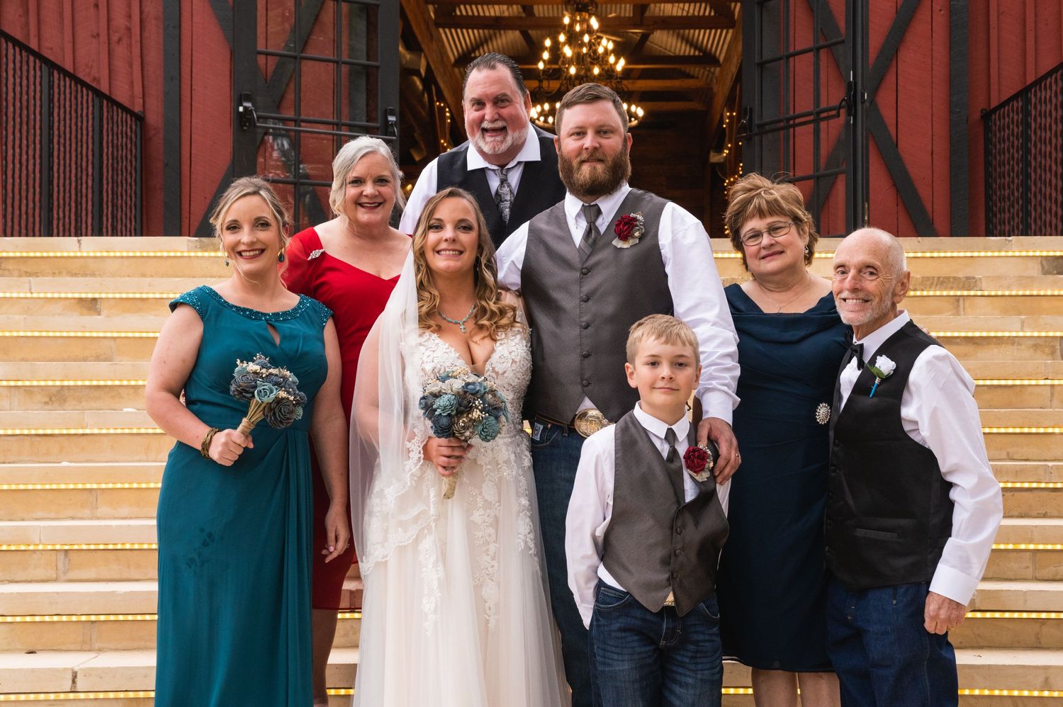 Small wedding family group portrait on wooden steps with rustic barn backdrop.