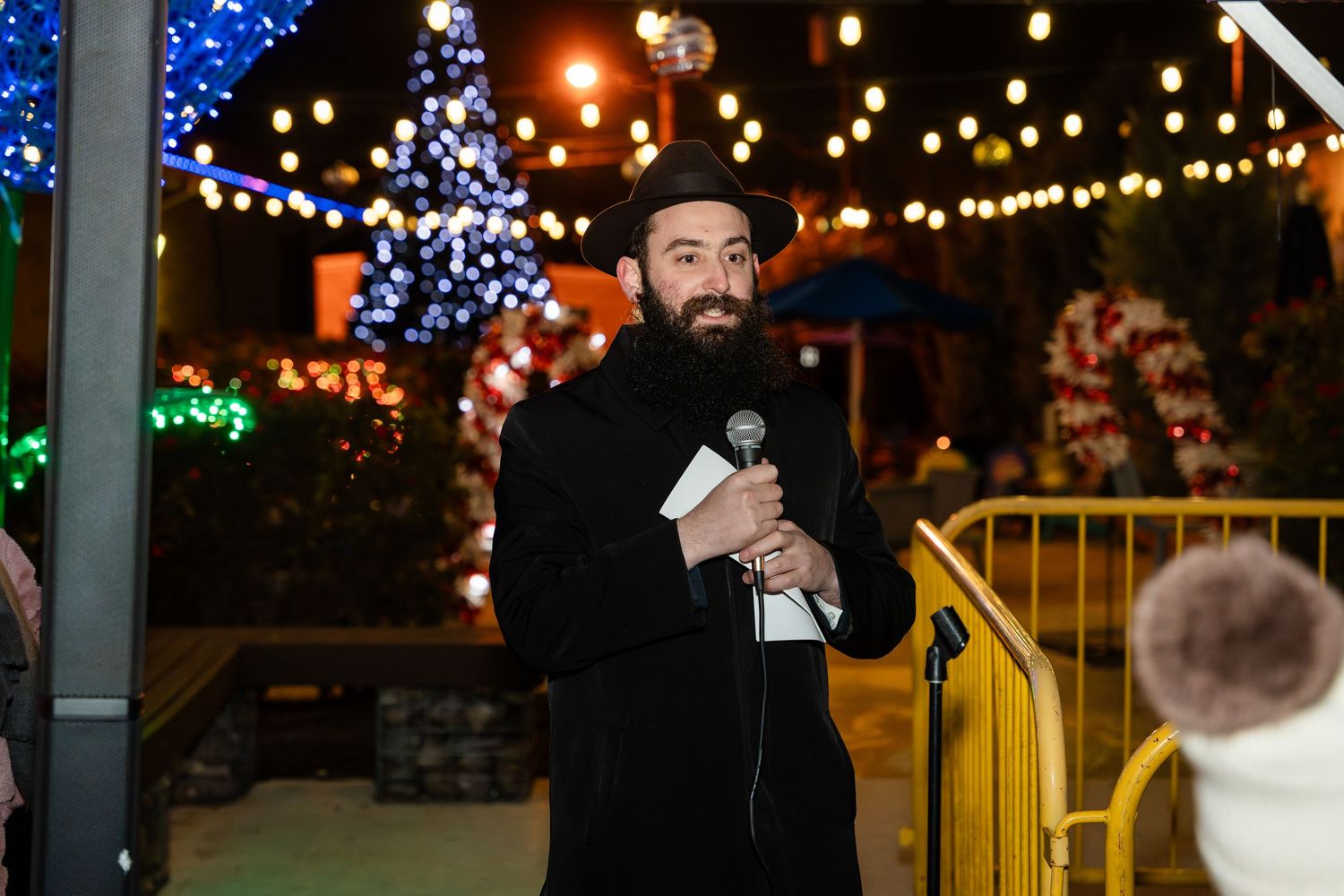 A crowd enjoys a festive outdoor event with colorful string lights and illuminated decorations creating a magical atmosphere.