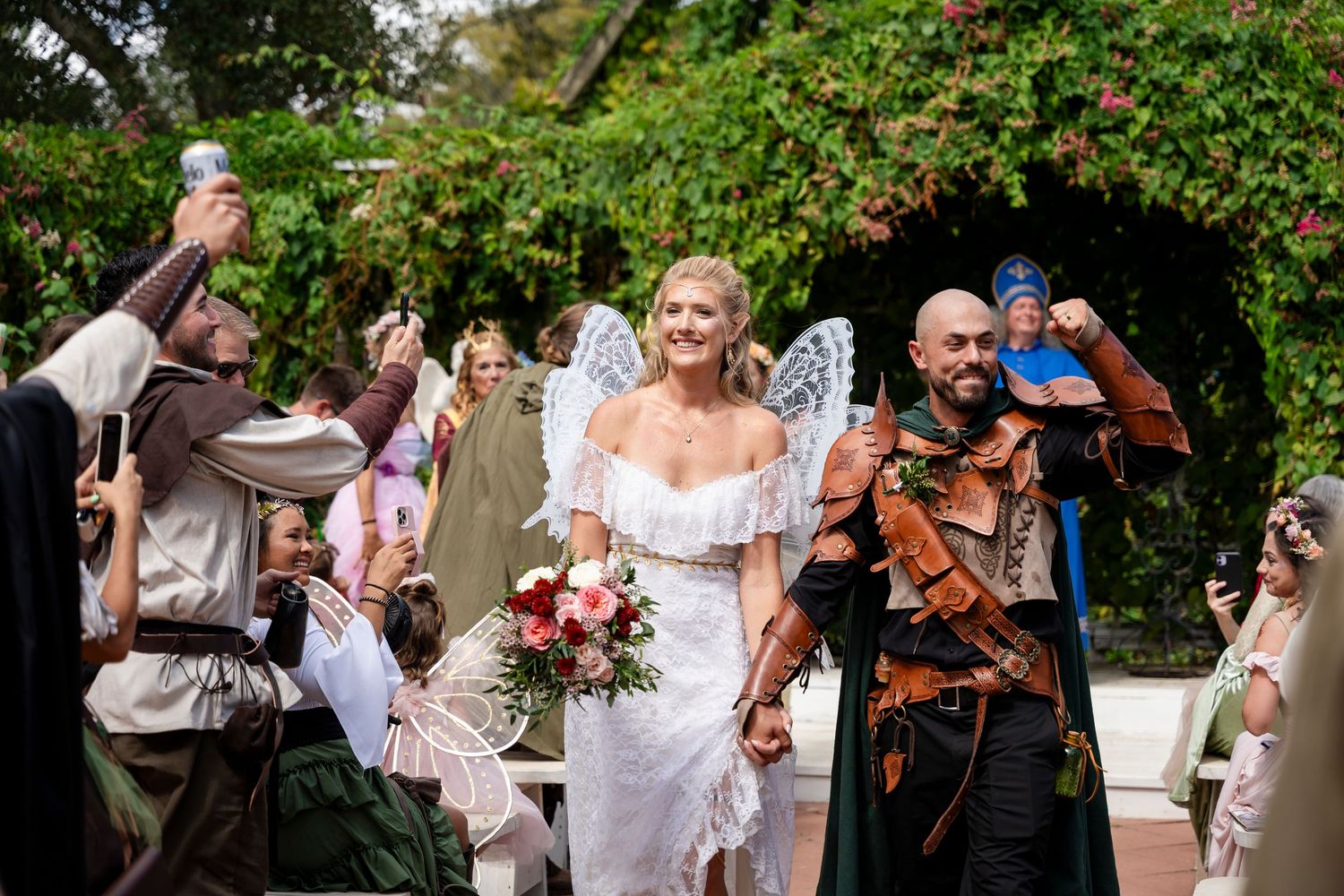 A joyful wedding celebration with guests in medieval and fantasy costumes in a garden setting.