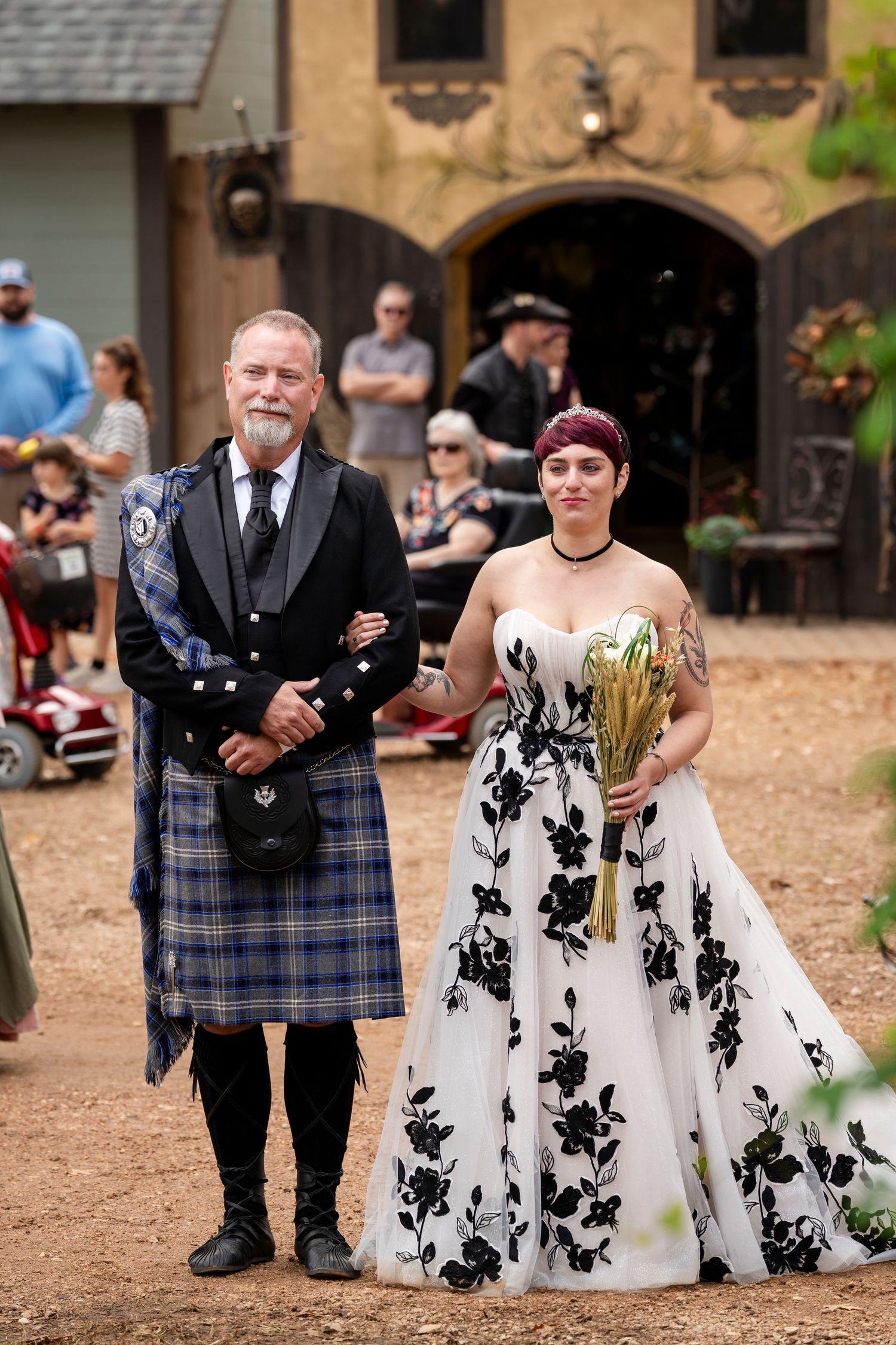 A wedding ceremony featuring a bride in a black and white floral dress with Scottish kilted attendants walking outdoors.