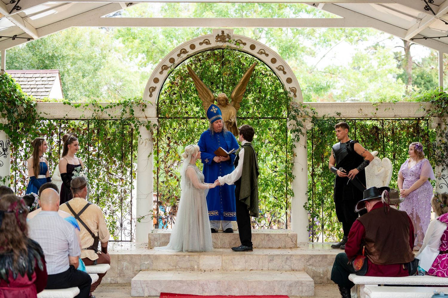 People gather under a white outdoor pavilion for a celebratory event in a garden setting.