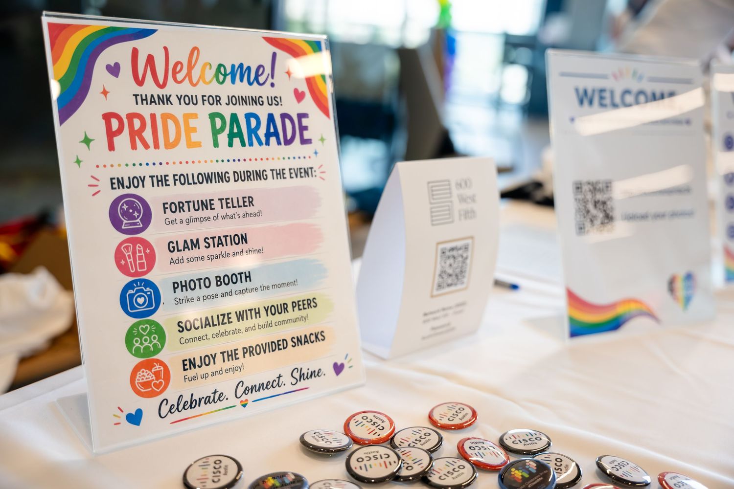 Colorful Pride Parade welcome sign displayed on table with rainbow decorations, buttons, and event activity listings.