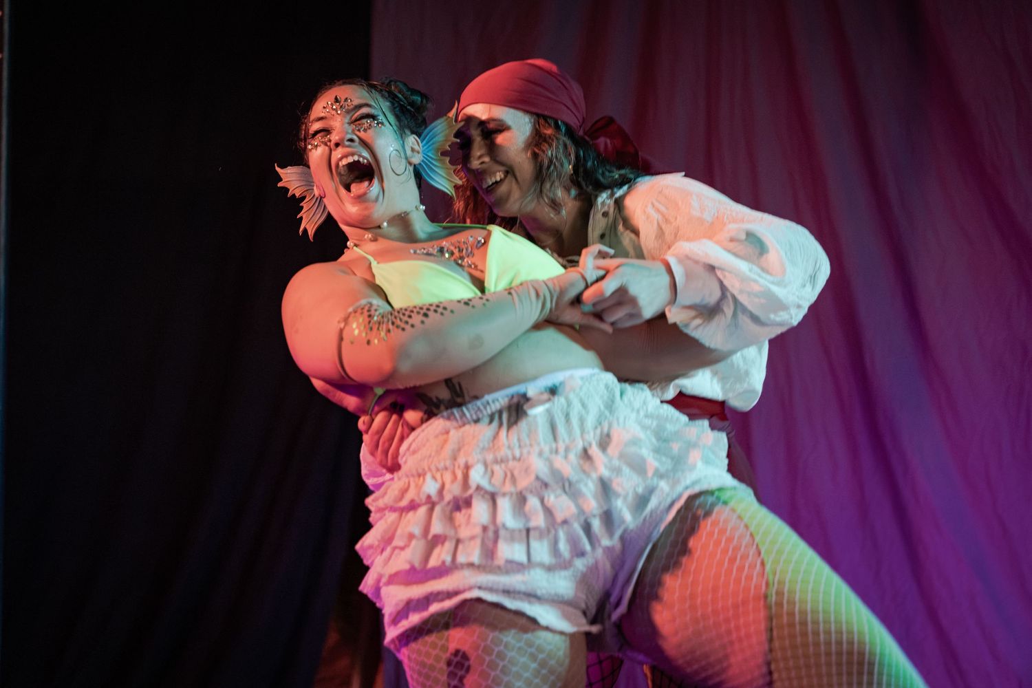 Two performers in pirate costumes dance dramatically on stage under colorful lighting.