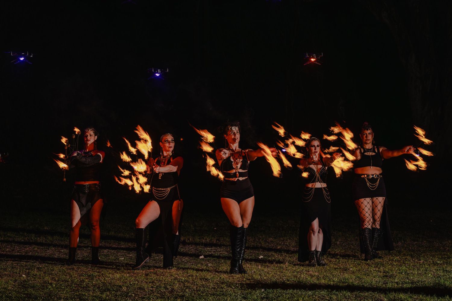 Fire dancers perform at night, wielding flaming props in a dramatic outdoor show.
