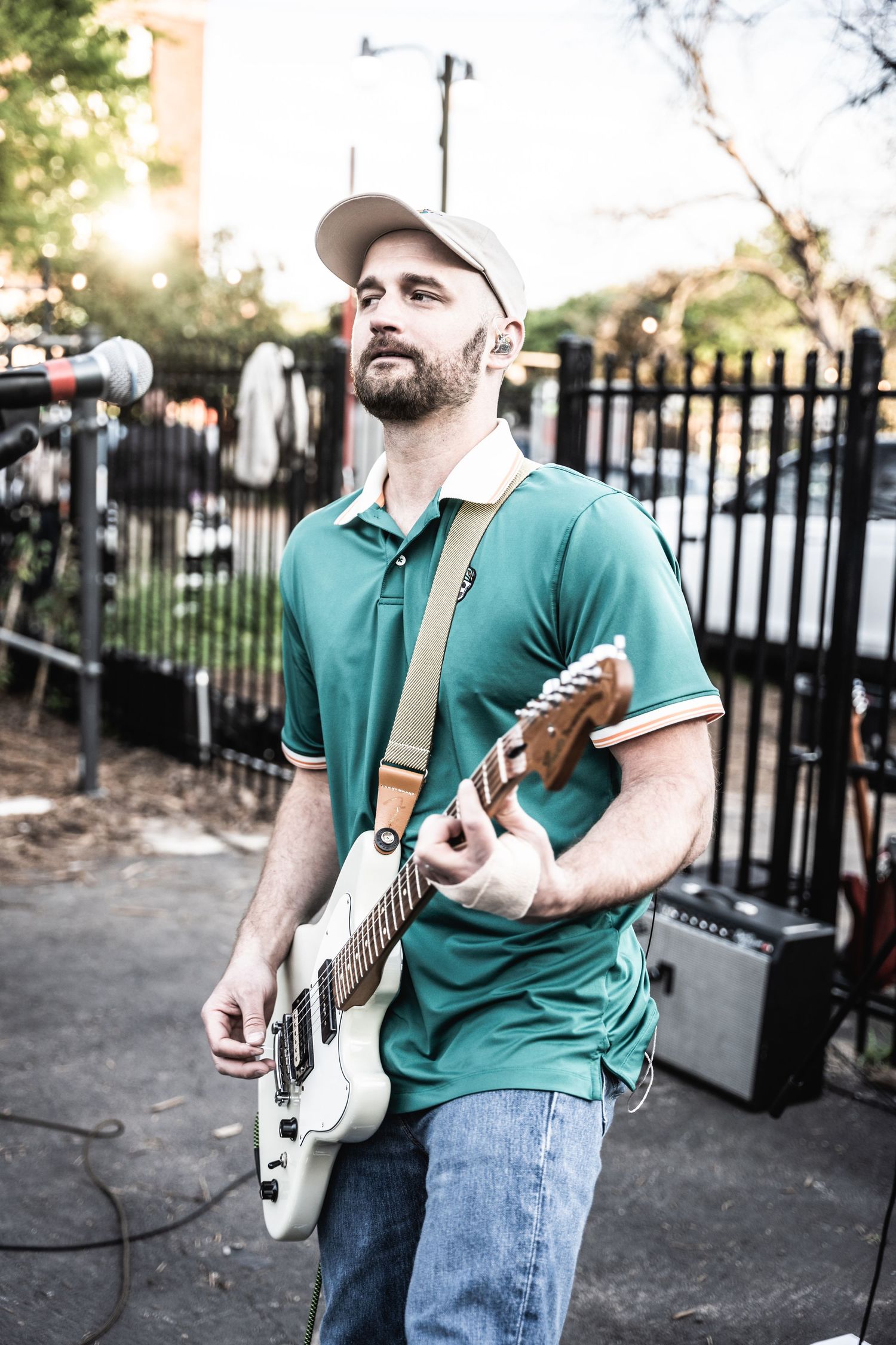 Musician in green polo shirt playing electric guitar at outdoor venue.