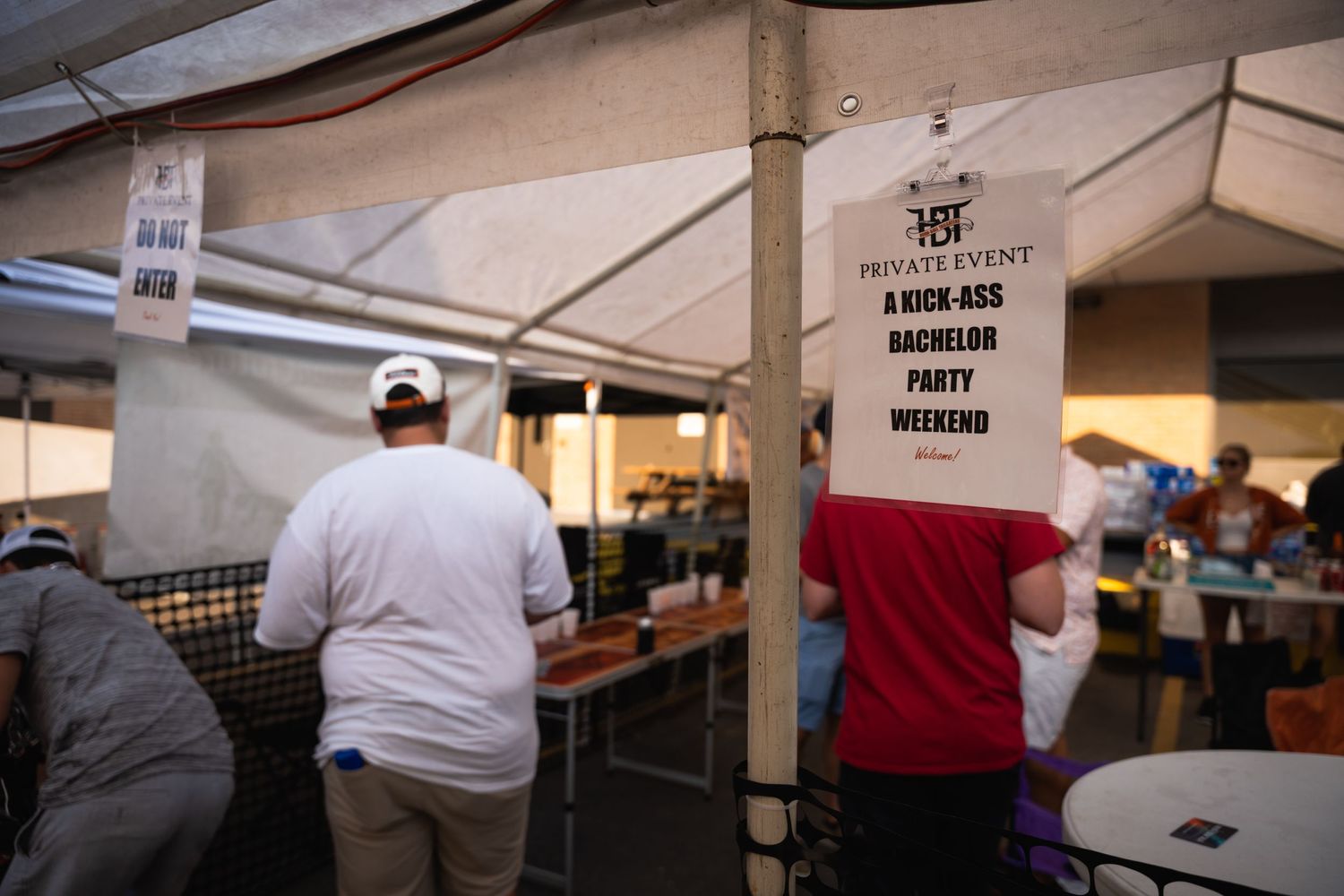 People gather under tents at a private event with signage visible in the background.