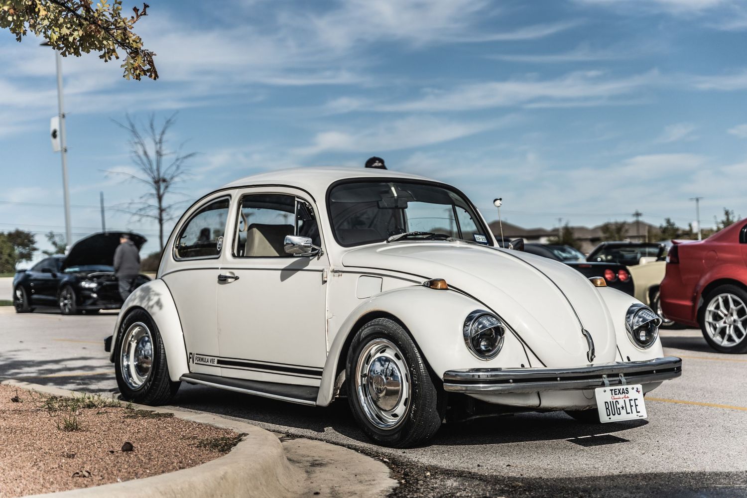 Lowered vintage Volkswagen Beetle in cream color parked at car show with custom wheels.