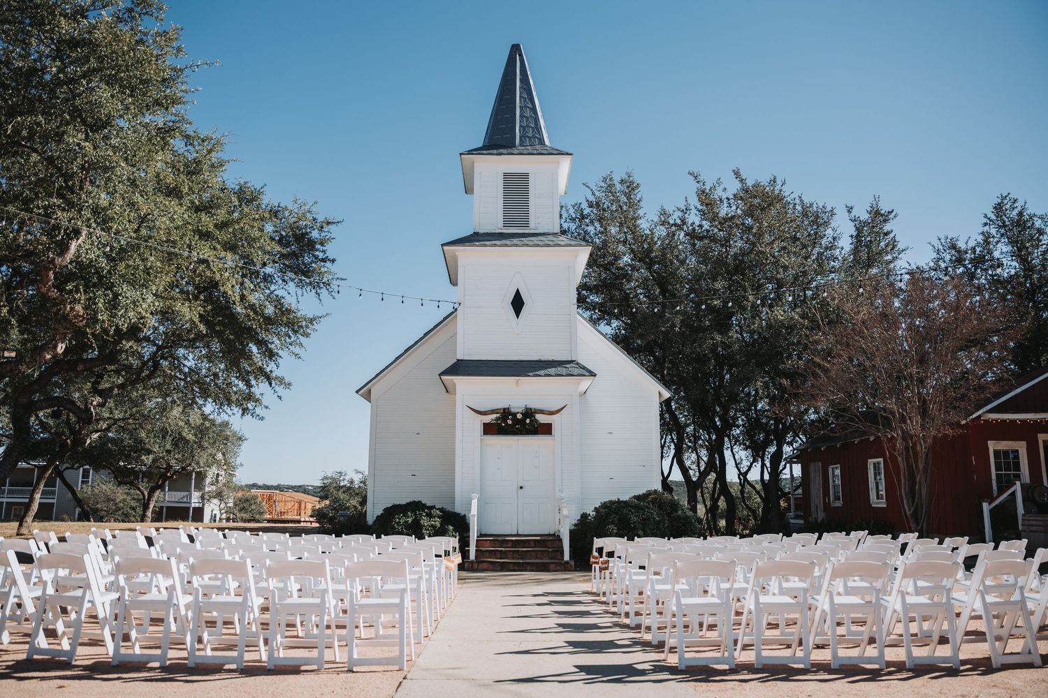 White chapel with steeple set up for outdoor wedding ceremony with rows of white chairs.