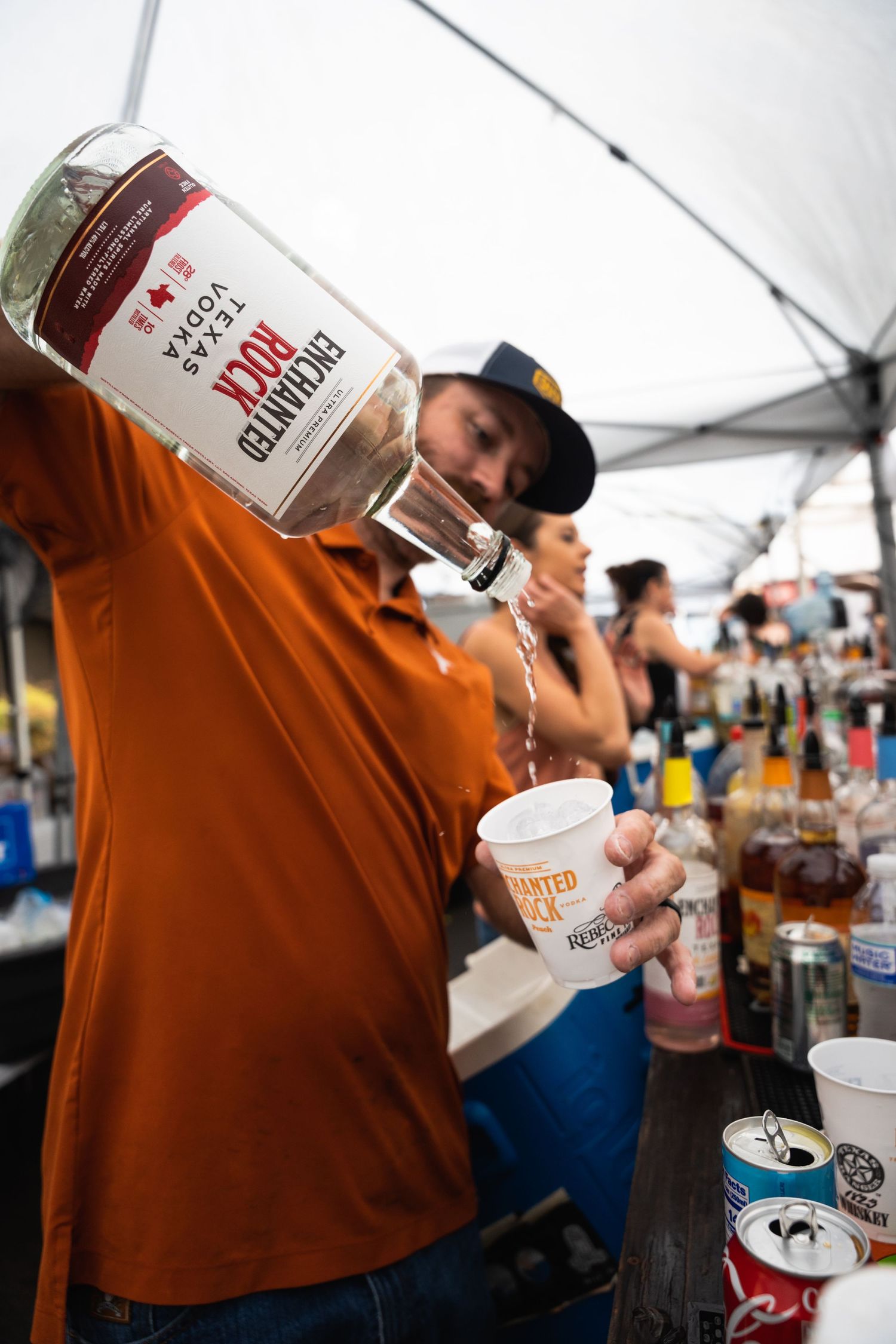 Bartender pours measured drink from large bottle at outdoor bar setup.