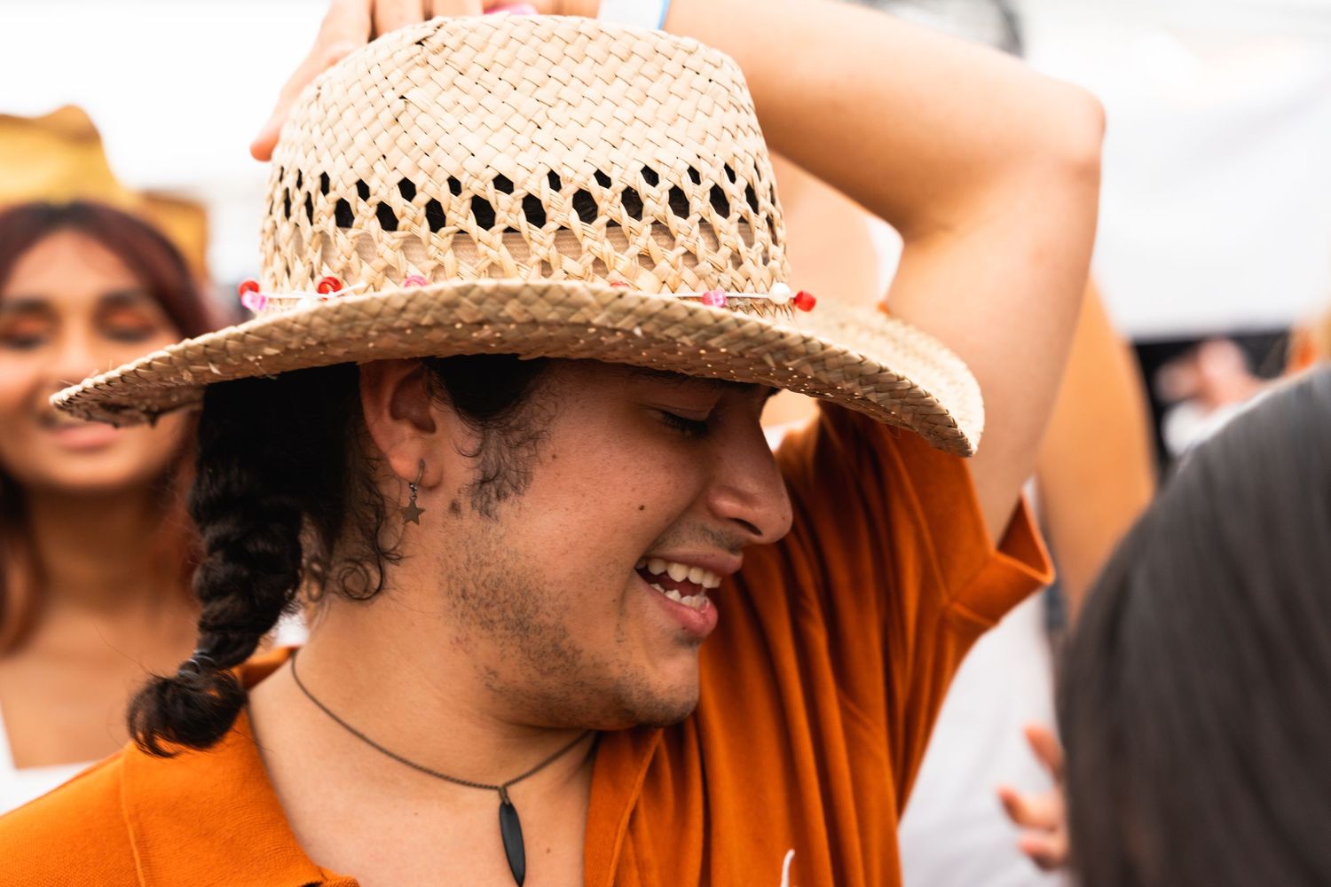 Person in orange shirt wearing a straw hat smiles at an outdoor festival.