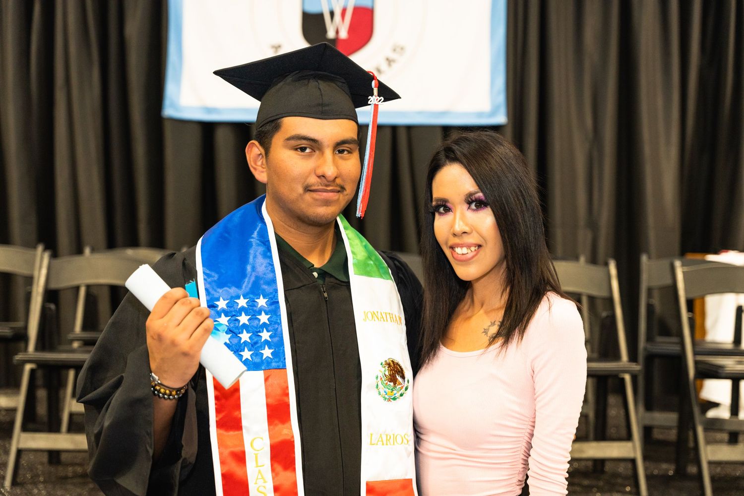 Graduate wearing American and Mexican flag stoles celebrates academic achievement.
