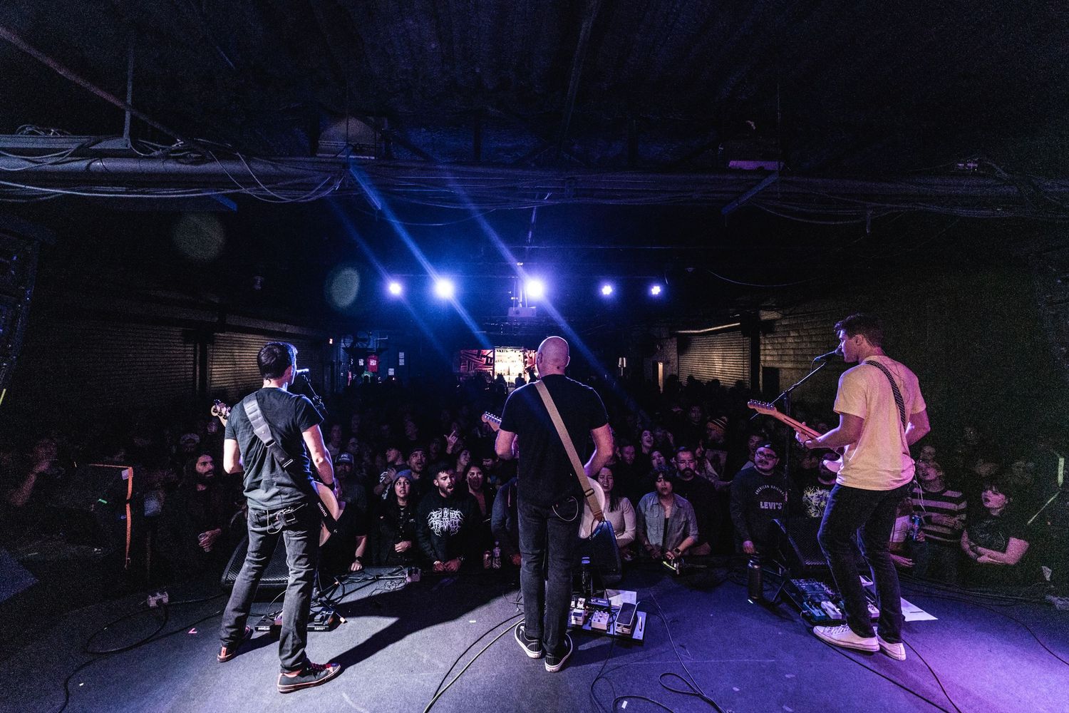 Band performs on dark stage with enthusiastic crowd in venue.