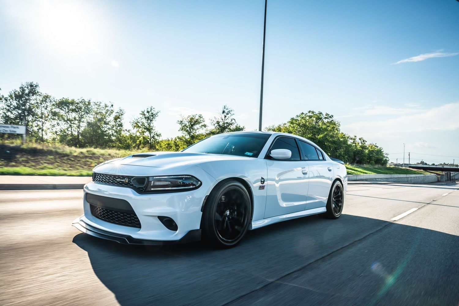 White Dodge Charger with performance modifications photographed on sunny road.