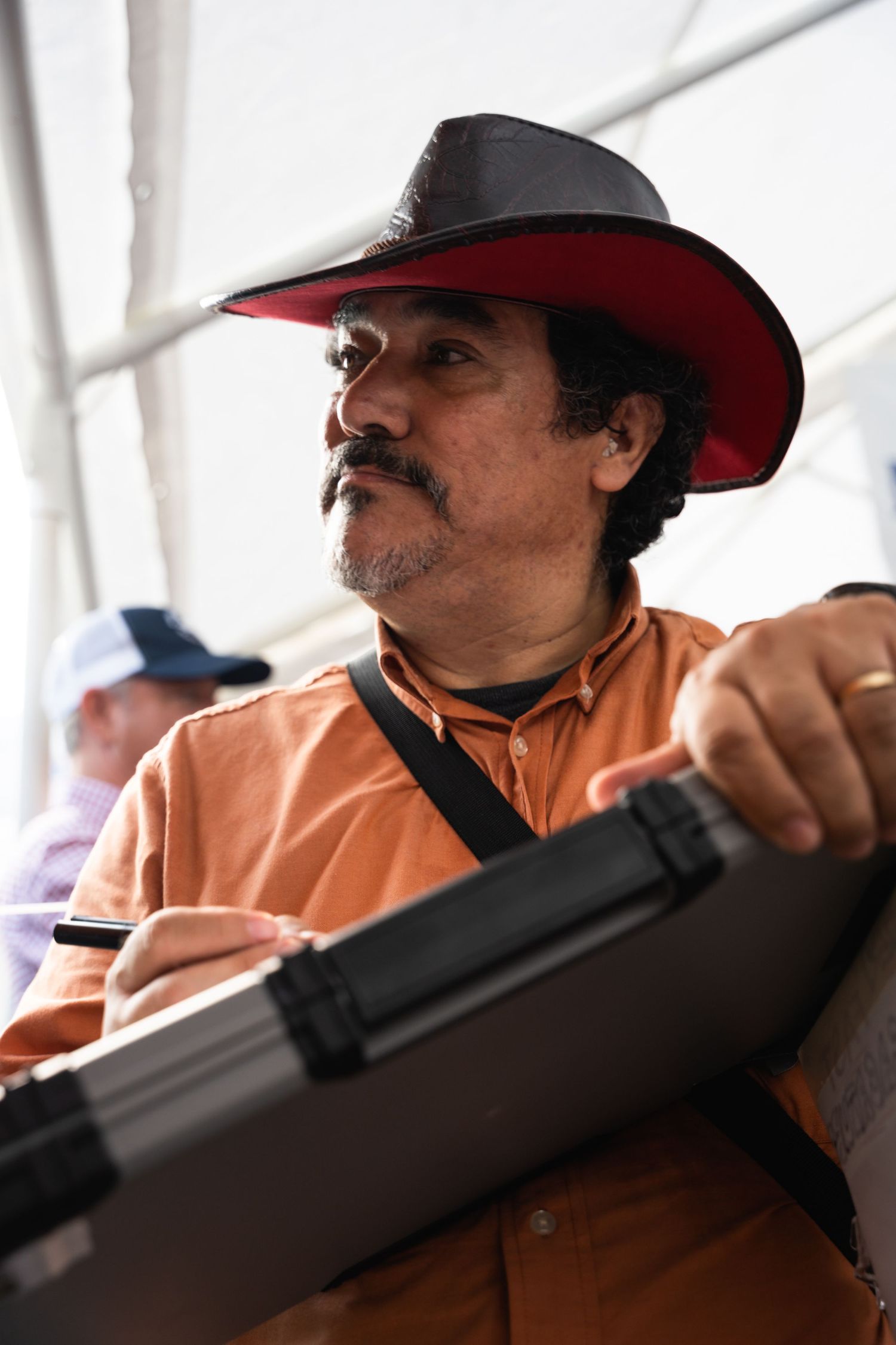 A person wearing an orange shirt and red-trimmed black cowboy hat holds a dark object.
